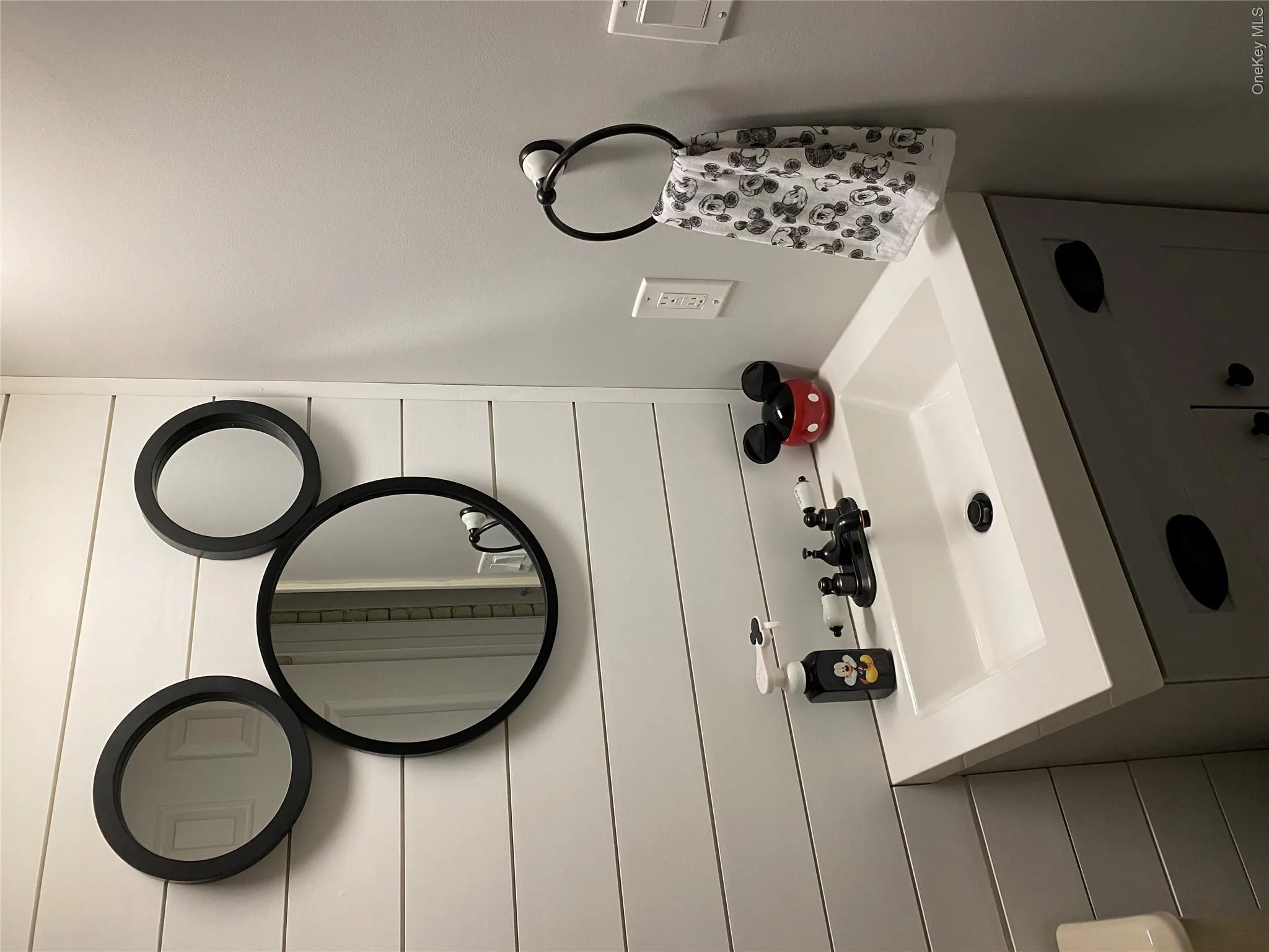 White shiplap accent wall with three circular mirrors, a white integrated sink, dark bronze faucet fixtures, and a gray vanity cabinet White shiplap accent wall with three circular mirrors, a white integrated sink, dark bronze faucet fixtures, and a gray vanity cabinet