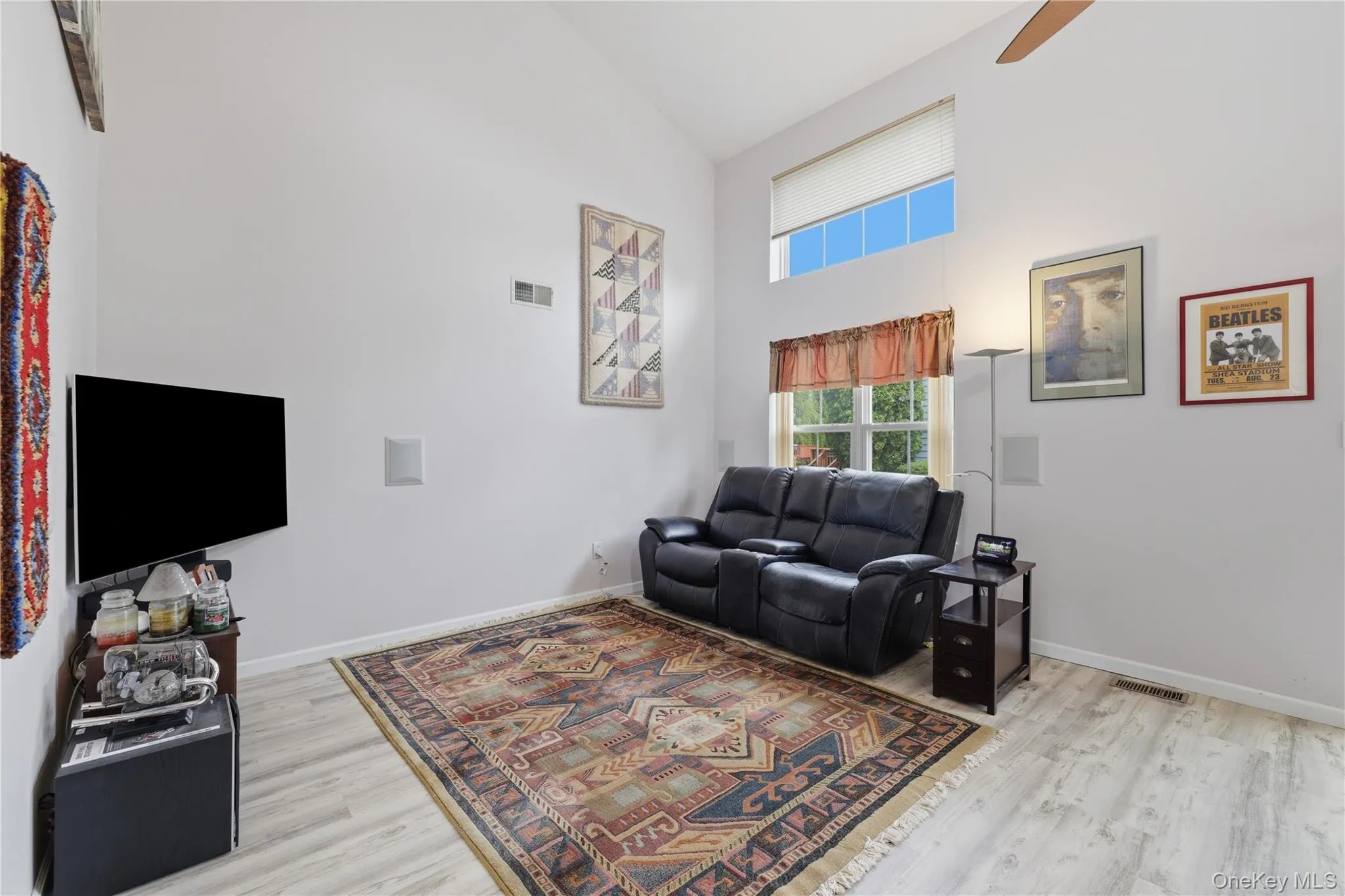 Room featuring high vaulted ceilings, light wood-finish flooring, and a large window with an upper transom Room featuring high vaulted ceilings, light wood-finish flooring, and a large window with an upper transom