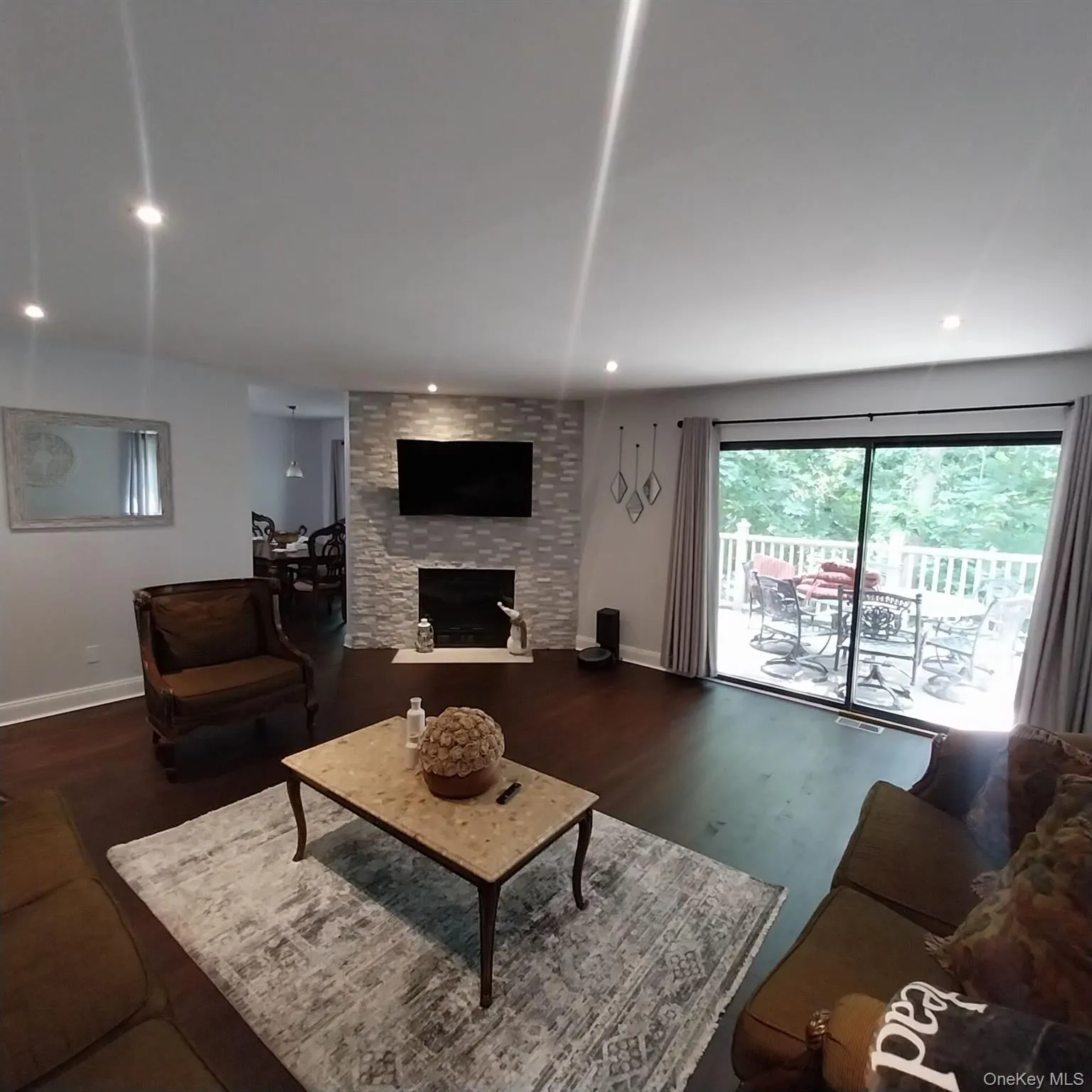 Spacious living area featuring wood-finish flooring, a stone-accented fireplace, and recessed lighting Spacious living area featuring wood-finish flooring, a stone-accented fireplace, and recessed lighting