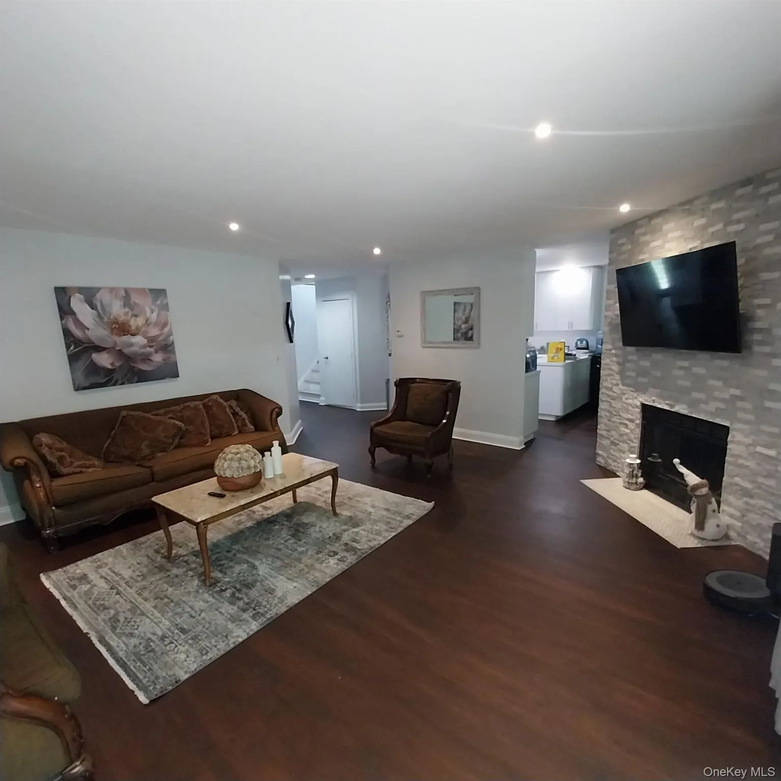 Spacious living area featuring rich wood-finish flooring, recessed lighting, and a stone-clad fireplace with a hearth Spacious living area featuring rich wood-finish flooring, recessed lighting, and a stone-clad fireplace with a hearth