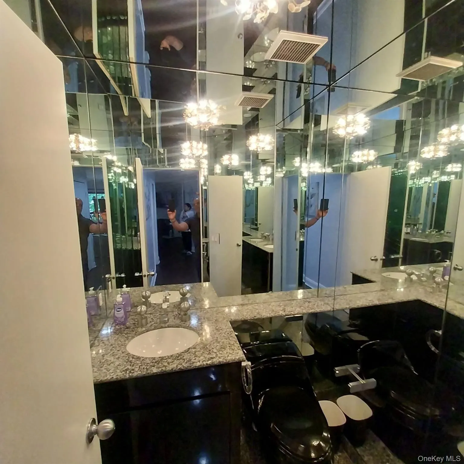 Bathroom featuring mirrored walls and ceiling, a vanity with a light-colored speckled countertop, an undermount sink, and a dark-toned cabinet base Bathroom featuring mirrored walls and ceiling, a vanity with a light-colored speckled countertop, an undermount sink, and a dark-toned cabinet base