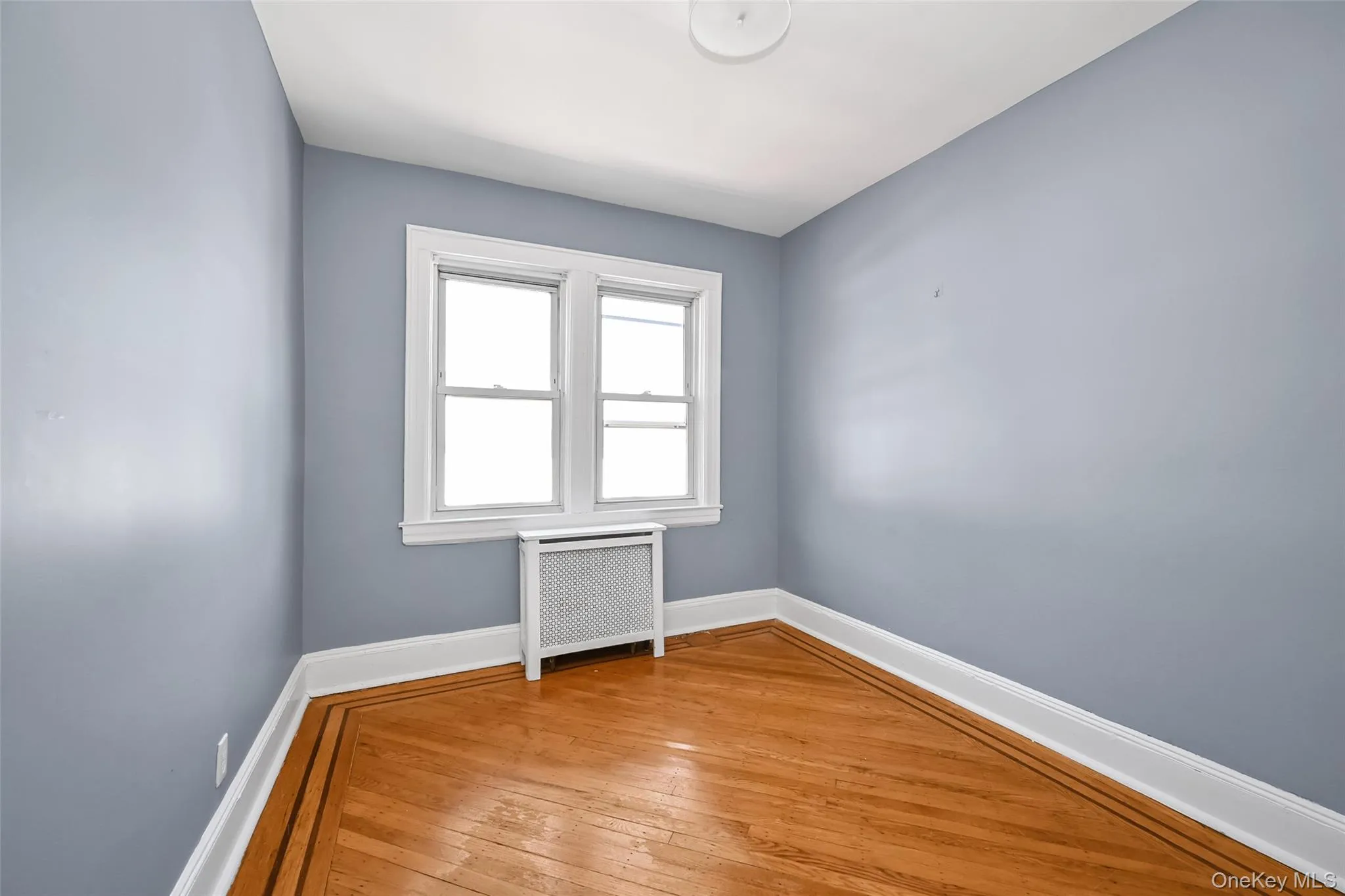 Room featuring wood-finish flooring with a perimeter inlay, white baseboards, and light blue walls Room featuring wood-finish flooring with a perimeter inlay, white baseboards, and light blue walls