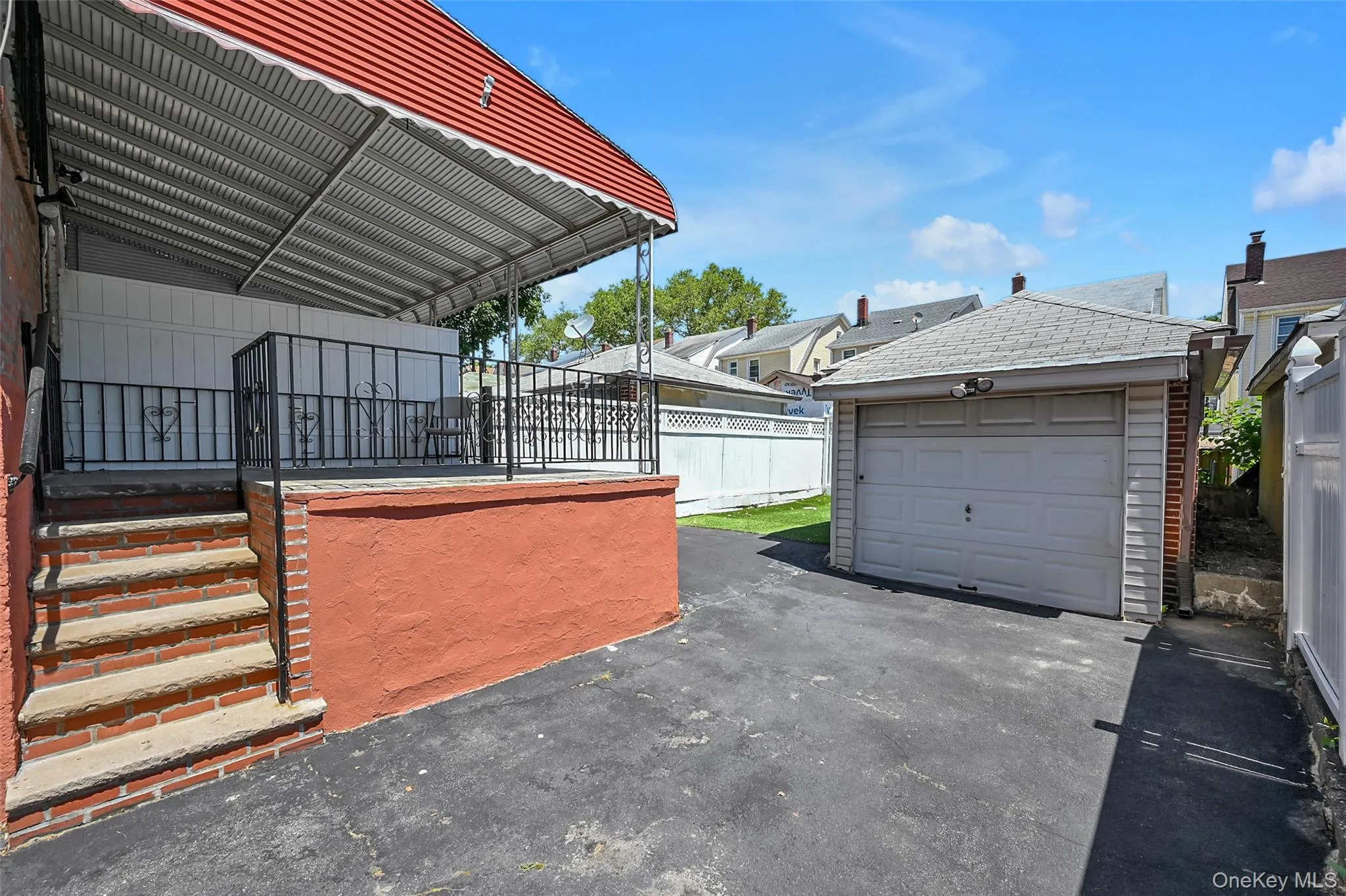 Brick exterior featuring a covered patio with metal railings, a white privacy fence, and a paved outdoor area Brick exterior featuring a covered patio with metal railings, a white privacy fence, and a paved outdoor area