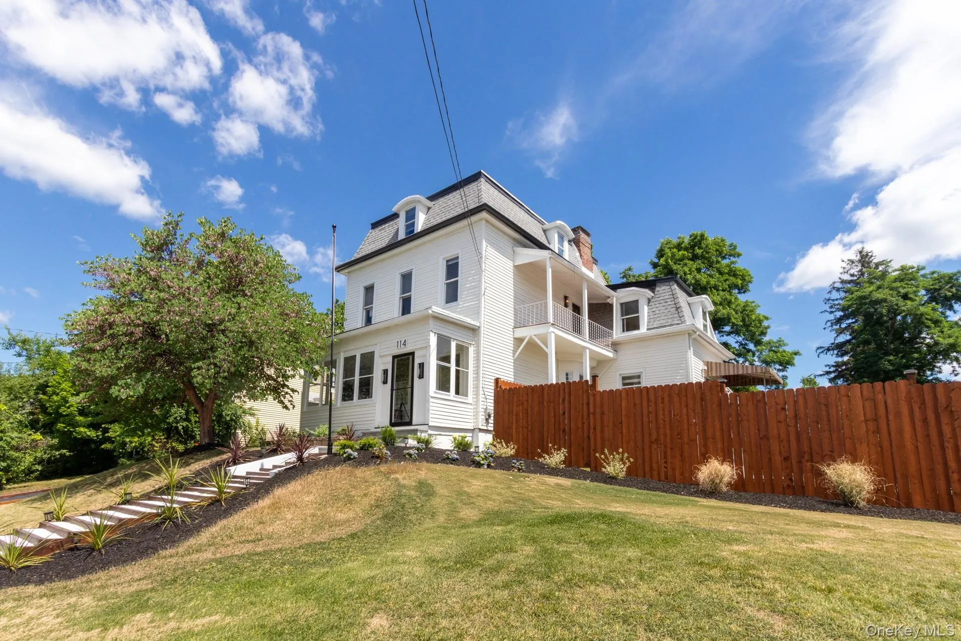 White multi-story residence featuring a mansard roof, dormer windows, and a front porch White multi-story residence featuring a mansard roof, dormer windows, and a front porch