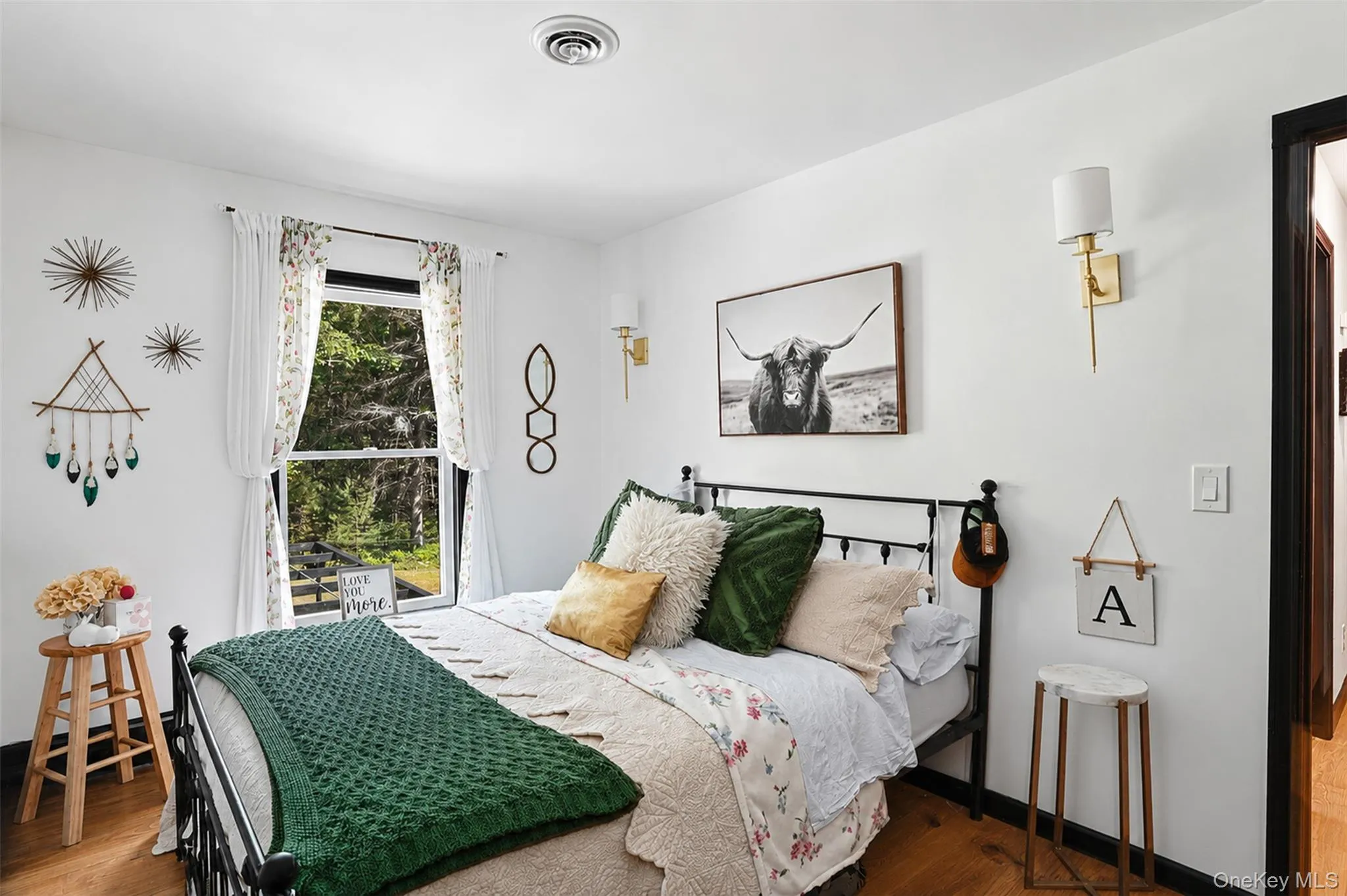Bedroom featuring wood-finish flooring, white walls, and a black wrought iron bed frame Bedroom featuring wood-finish flooring, white walls, and a black wrought iron bed frame