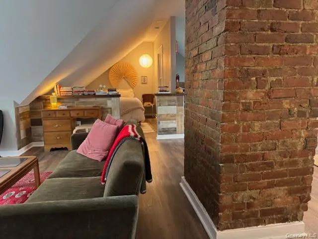 Bedroom featuring wood finished floors, vaulted ceiling, and brick wall Bedroom featuring wood finished floors, vaulted ceiling, and brick wall