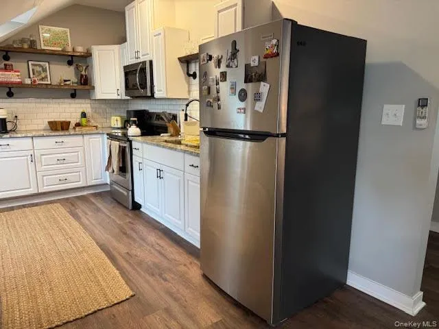 Kitchen featuring appliances with stainless steel finishes, dark wood-style floors, decorative backsplash, white cabinets, and lofted ceiling Kitchen featuring appliances with stainless steel finishes, dark wood-style floors, decorative backsplash, white cabinets, and lofted ceiling