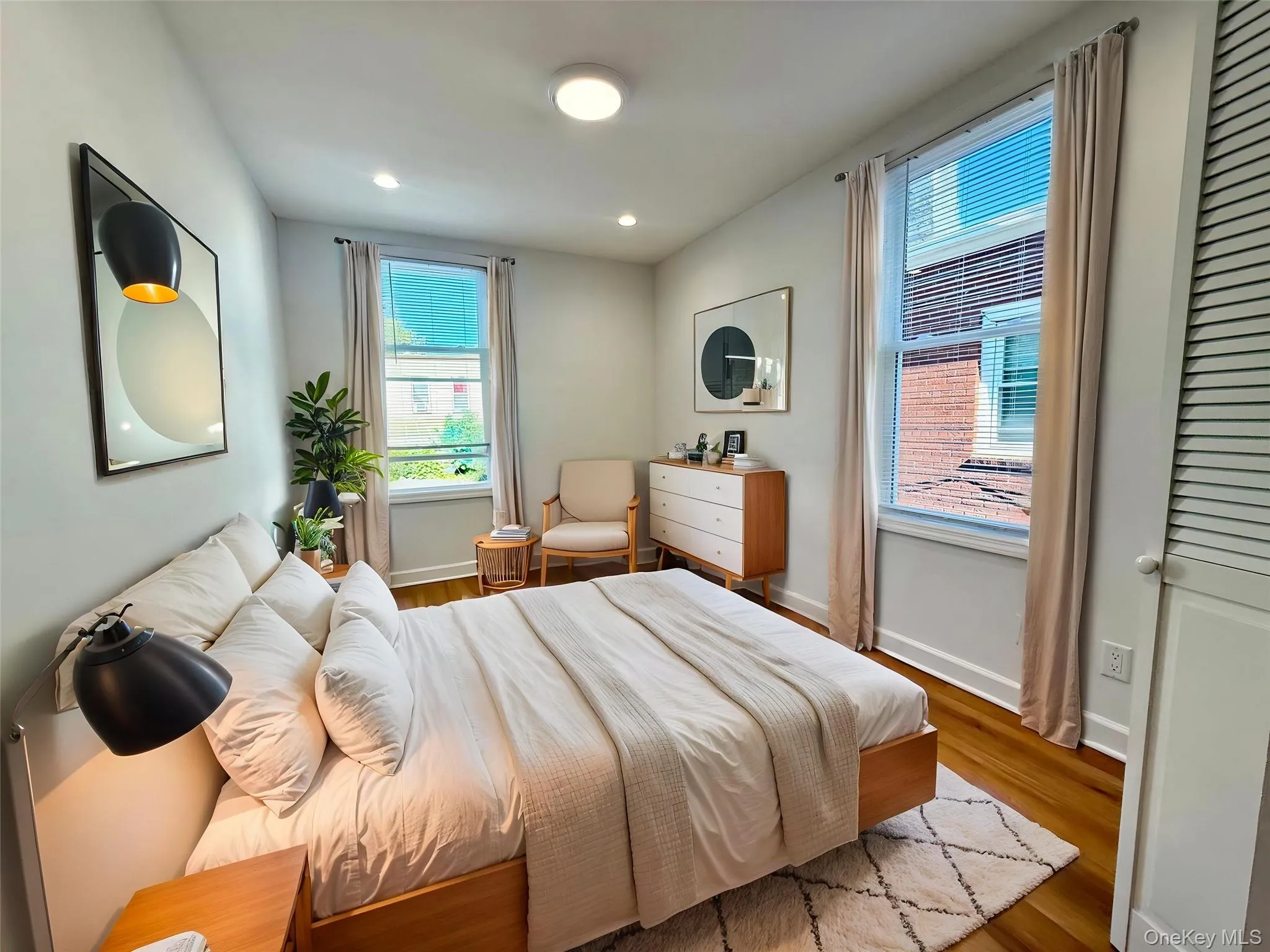 Bedroom featuring two large windows with blinds and neutral curtains, recessed ceiling lighting, and wood-finish flooring Bedroom featuring two large windows with blinds and neutral curtains, recessed ceiling lighting, and wood-finish flooring