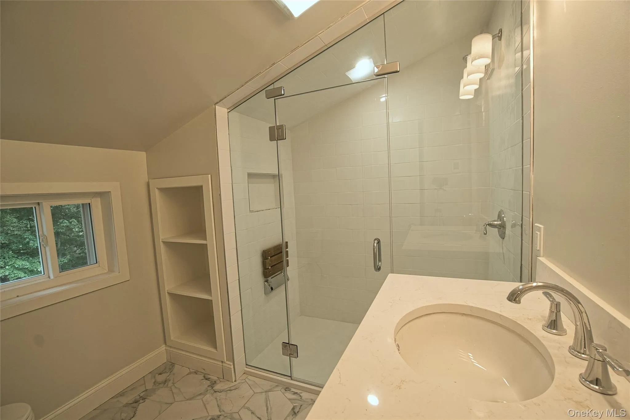 Contemporary bathroom featuring a clear glass walk-in shower with a built-in bench, a single vanity with an integrated sink and chrome faucet, and white tile flooring Contemporary bathroom featuring a clear glass walk-in shower with a built-in bench, a single vanity with an integrated sink and chrome faucet, and white tile flooring