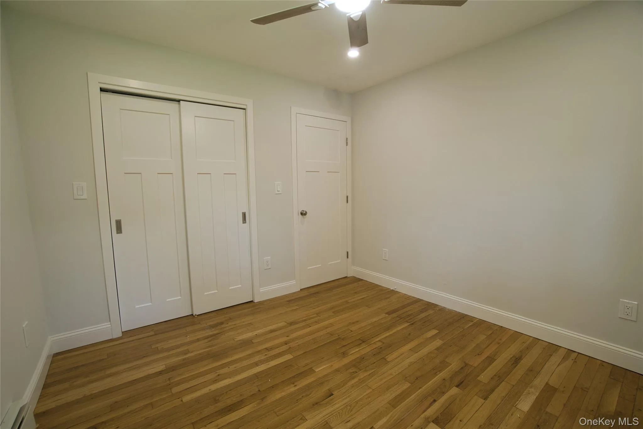 Bedroom featuring wood-finish flooring, a ceiling fan with integrated lighting, and a closet with sliding panel doors Bedroom featuring wood-finish flooring, a ceiling fan with integrated lighting, and a closet with sliding panel doors