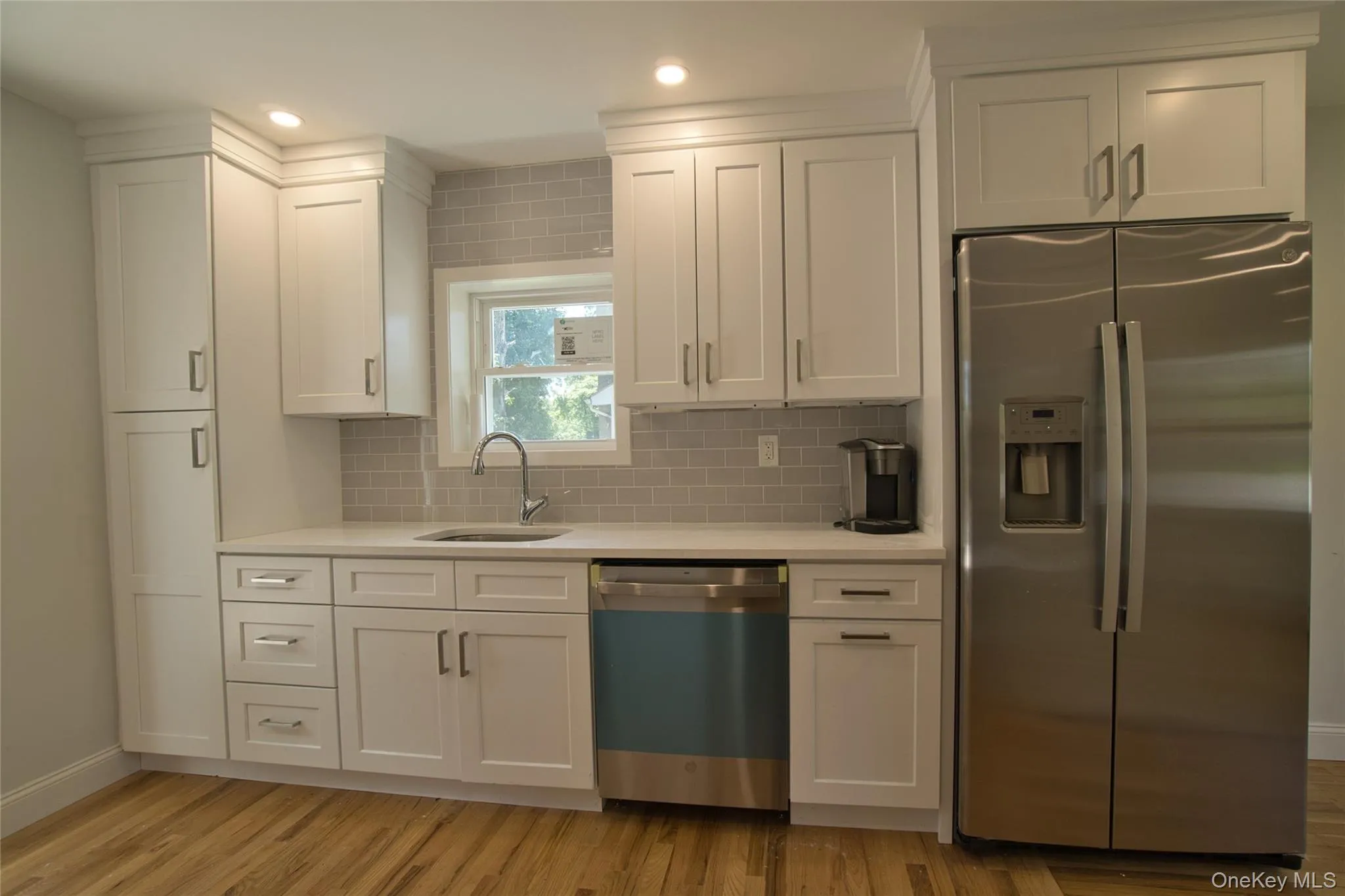 Modern kitchen featuring white shaker cabinetry, stainless steel appliances, a white solid surface countertop, and a light gray subway tile backsplash Modern kitchen featuring white shaker cabinetry, stainless steel appliances, a white solid surface countertop, and a light gray subway tile backsplash