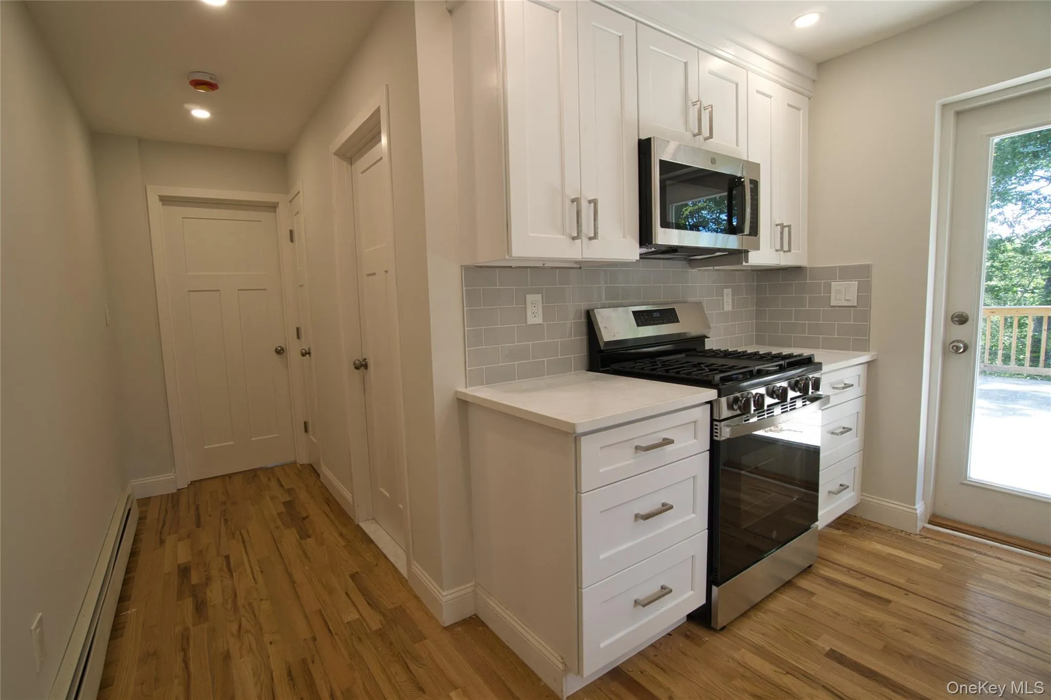 Kitchen featuring white shaker cabinetry, stainless steel appliances, light subway tile backsplash, and light-toned countertops Kitchen featuring white shaker cabinetry, stainless steel appliances, light subway tile backsplash, and light-toned countertops