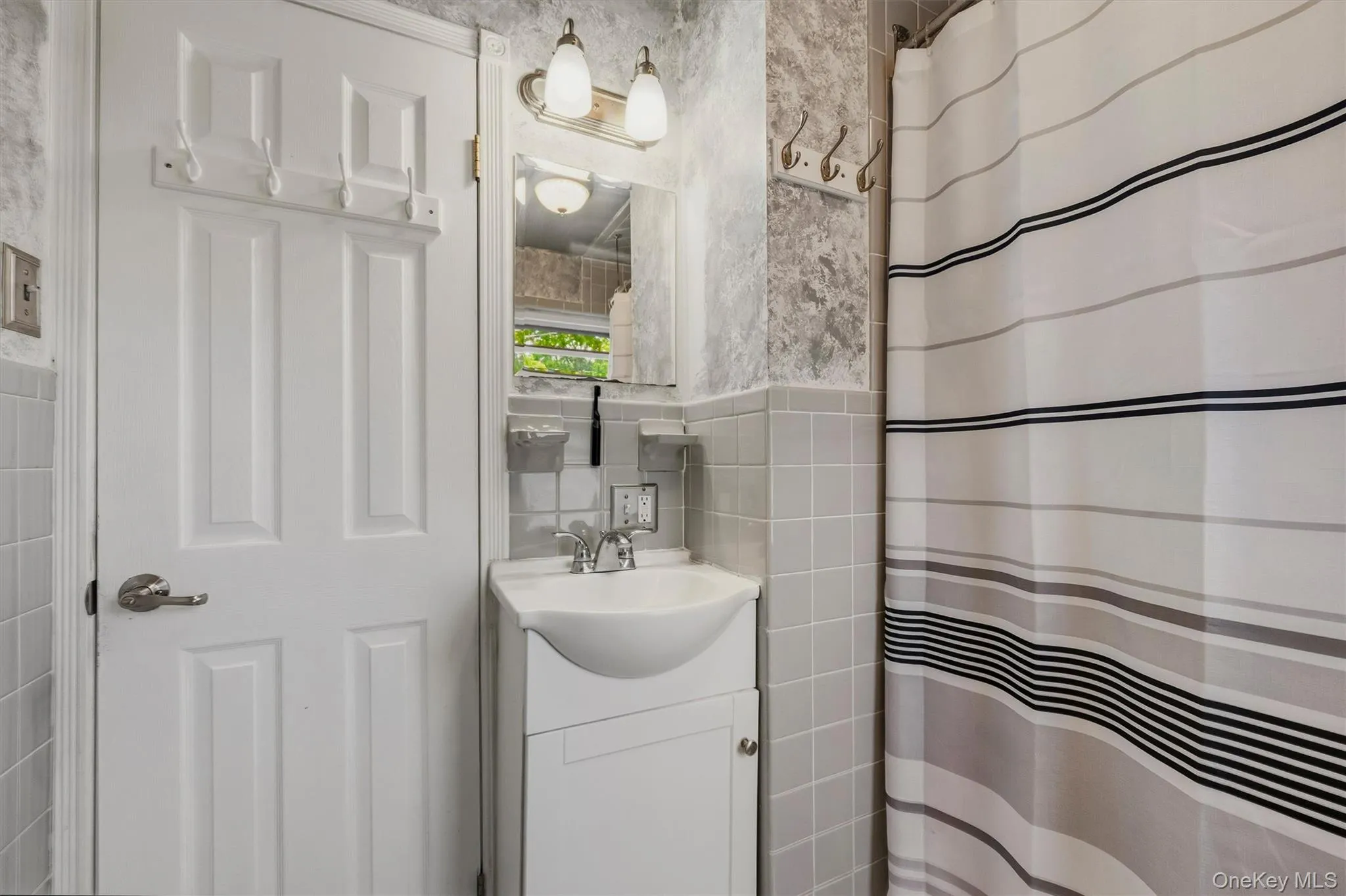 Bathroom featuring a white four-panel door, pedestal sink with integrated storage, chrome fixtures, and a vanity light fixture Bathroom featuring a white four-panel door, pedestal sink with integrated storage, chrome fixtures, and a vanity light fixture