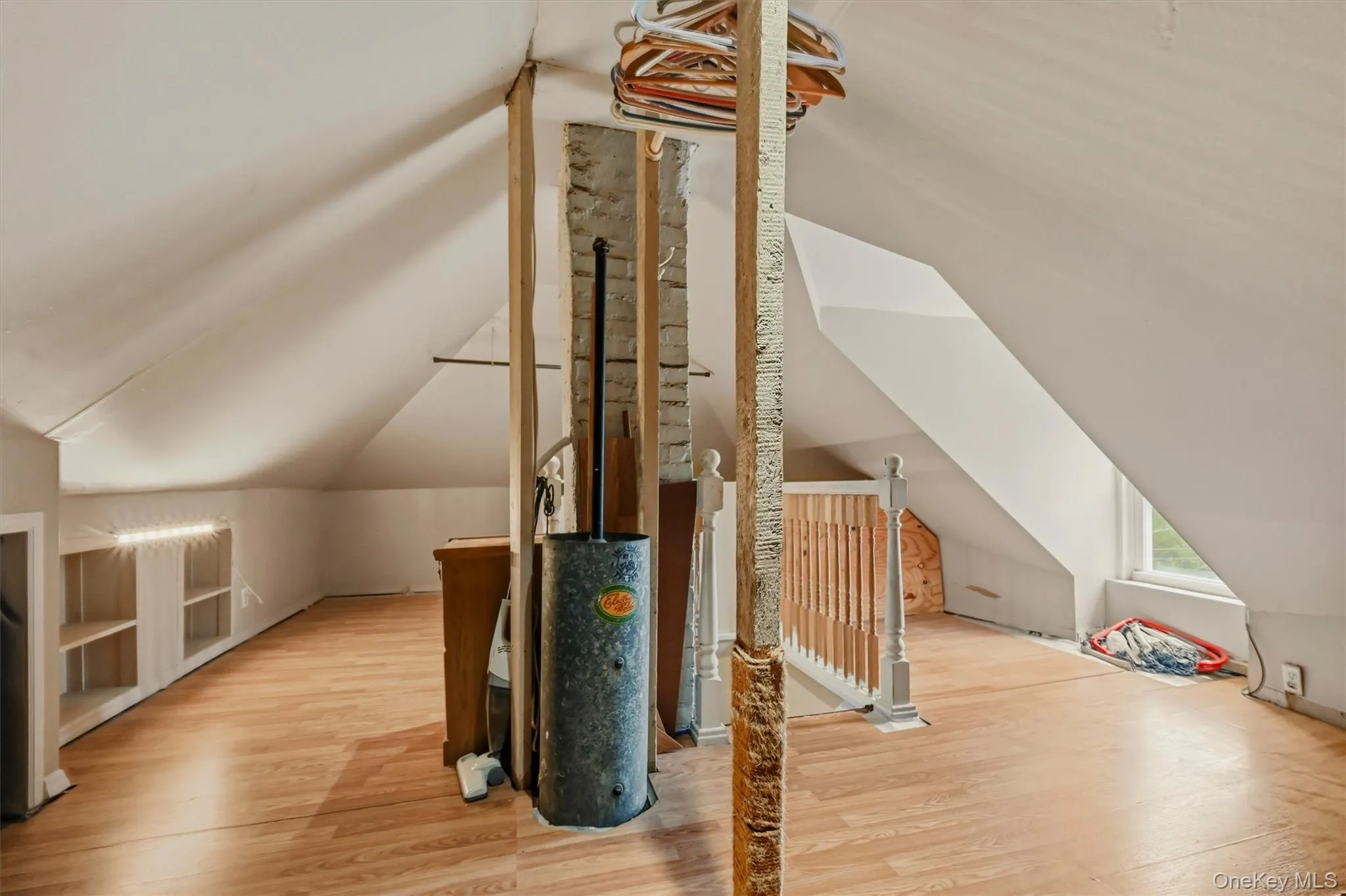 Attic space featuring wood-finish flooring, exposed structural beams, a partial wood-finish banister, and built-in shelving with integrated lighting Attic space featuring wood-finish flooring, exposed structural beams, a partial wood-finish banister, and built-in shelving with integrated lighting