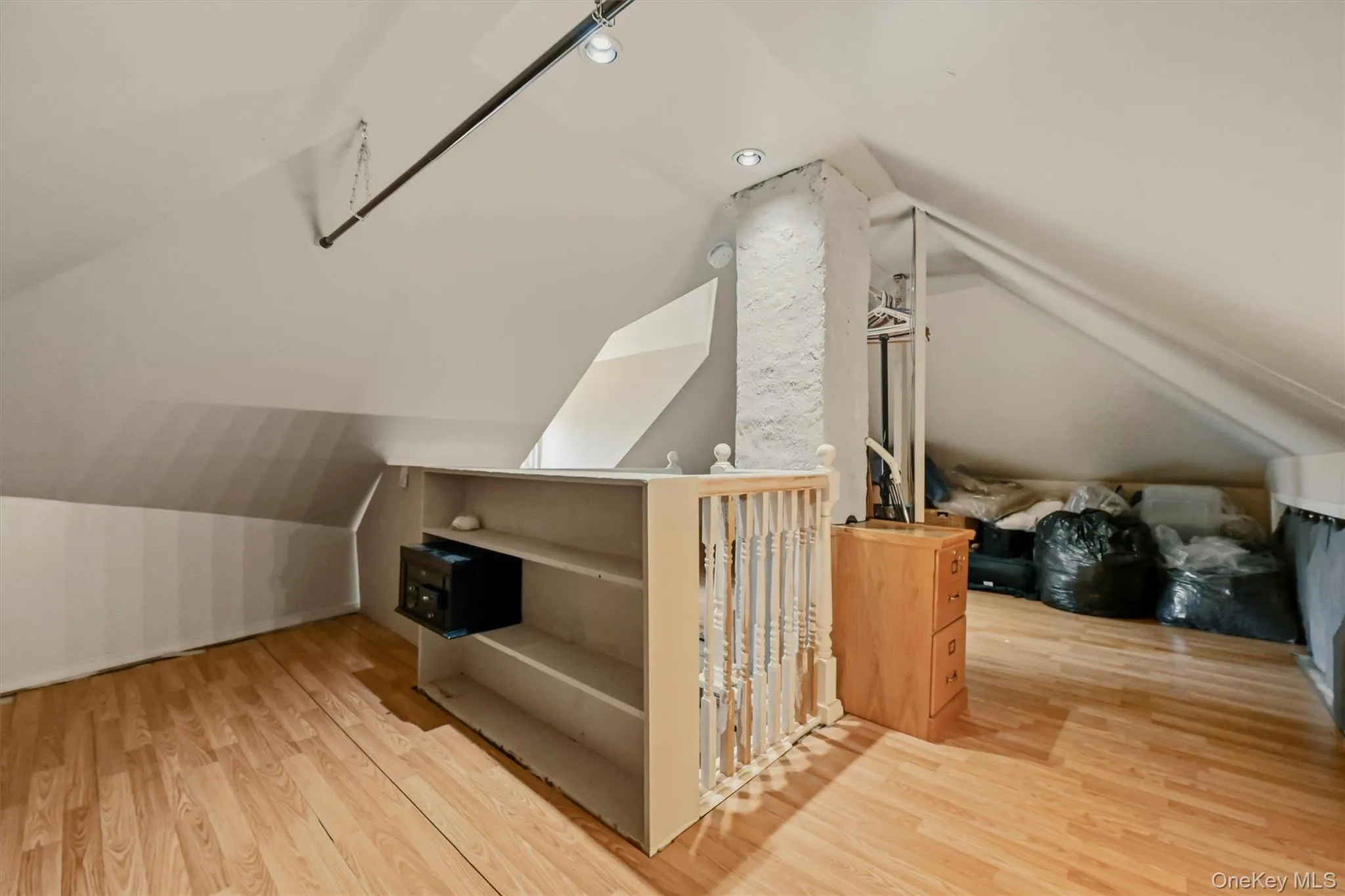 Attic room featuring wood-finish flooring, white sloped ceilings, and built-in shelving Attic room featuring wood-finish flooring, white sloped ceilings, and built-in shelving