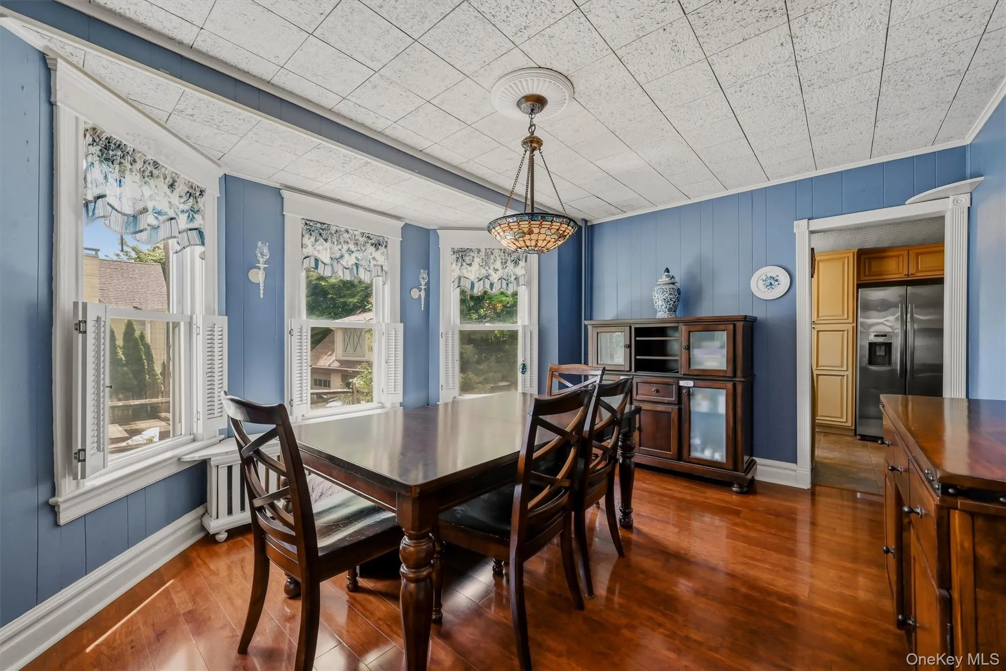 Dining area with wood-finish flooring, a bay window with multiple panes, and a decorative ceiling fixture Dining area with wood-finish flooring, a bay window with multiple panes, and a decorative ceiling fixture