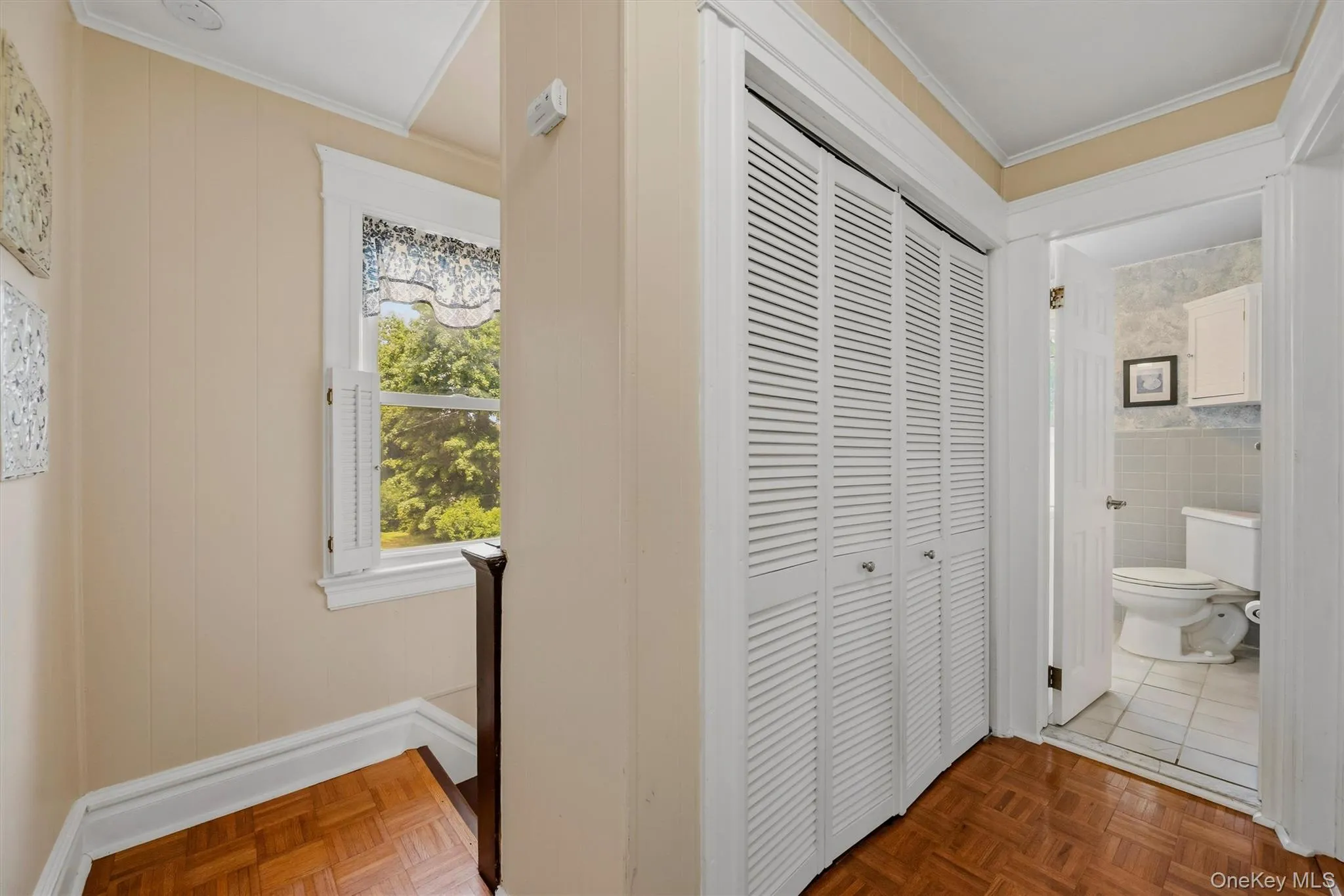 Hallway featuring wood-finish parquet flooring, paneled walls, and a window with white louvered shutters Hallway featuring wood-finish parquet flooring, paneled walls, and a window with white louvered shutters