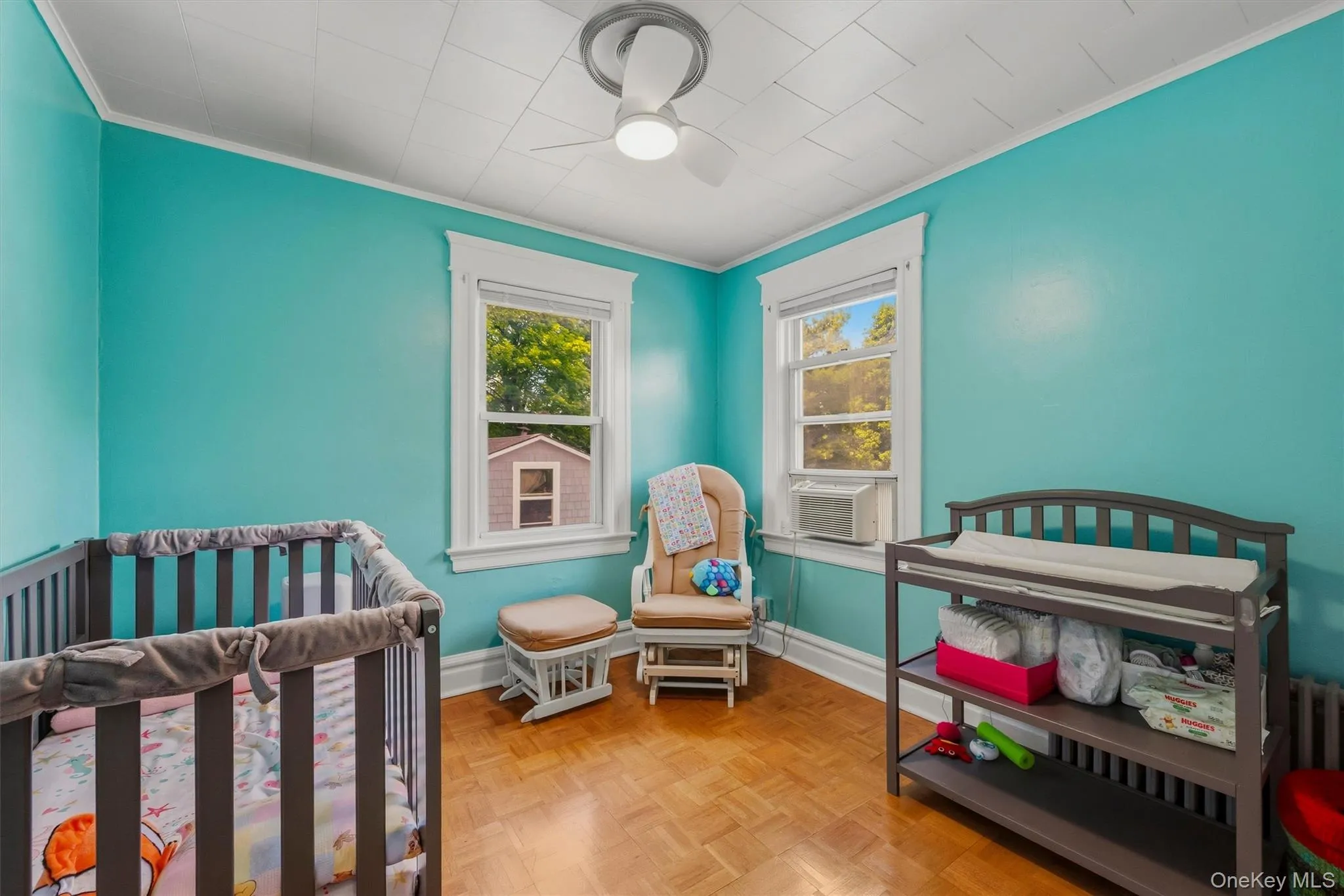 Room featuring wood-finish parquet flooring, two windows with white trim, a ceiling fan with integrated lighting, and crown molding Room featuring wood-finish parquet flooring, two windows with white trim, a ceiling fan with integrated lighting, and crown molding
