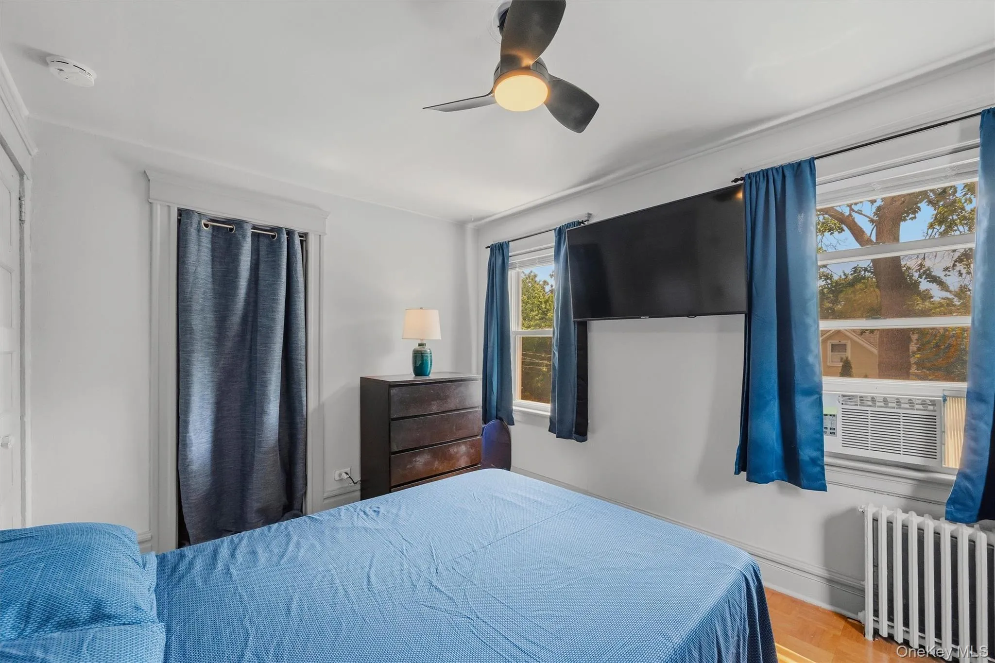 Bedroom featuring wood-finish flooring, a ceiling fan with integrated lighting, and multiple windows with white trim Bedroom featuring wood-finish flooring, a ceiling fan with integrated lighting, and multiple windows with white trim