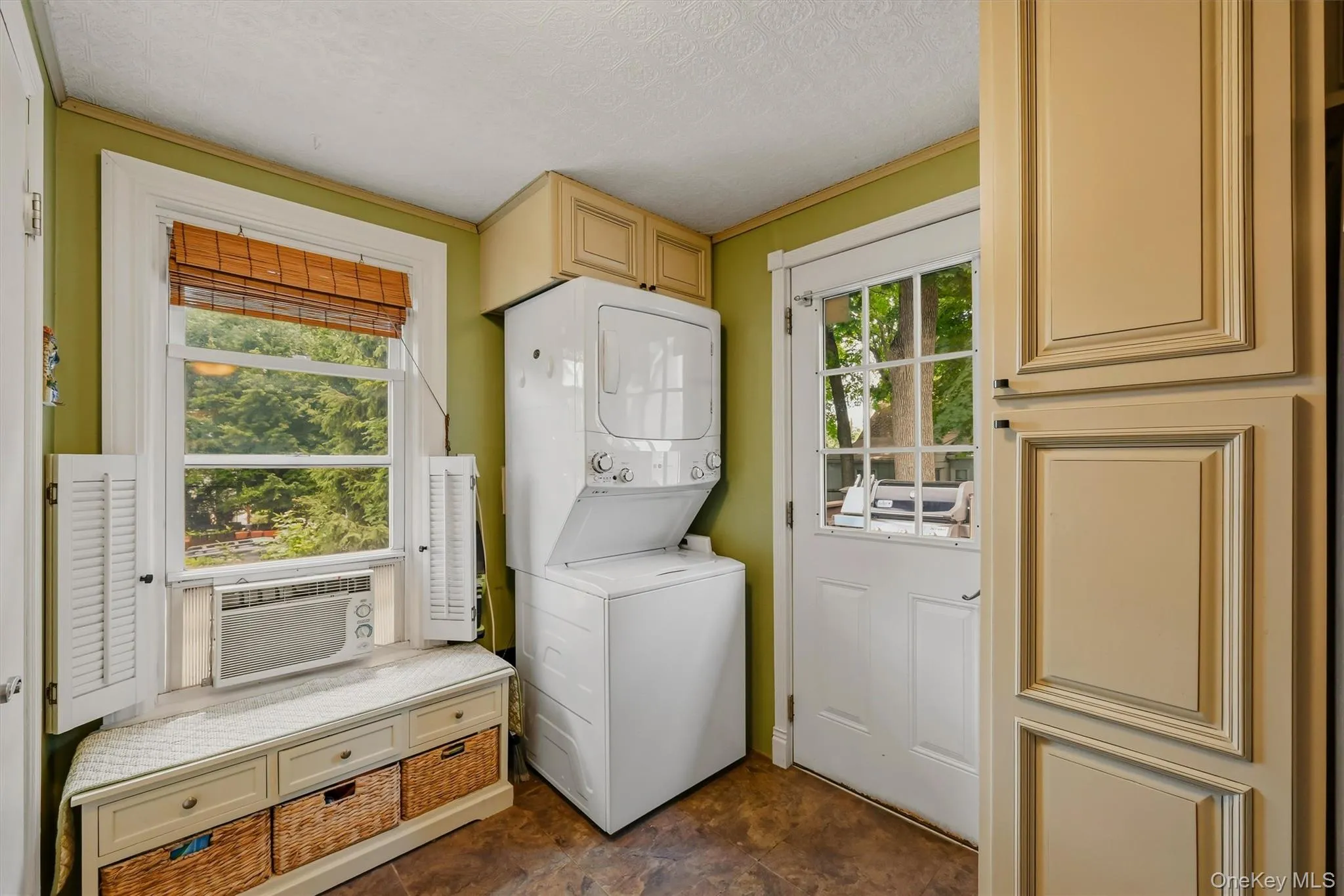 Functional utility space featuring a built-in stacked washer and dryer, shaker-style cabinetry, and a window with white shutters Functional utility space featuring a built-in stacked washer and dryer, shaker-style cabinetry, and a window with white shutters