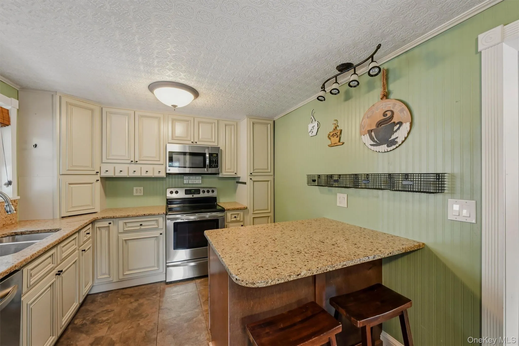 Kitchen featuring stainless steel appliances, cream-colored cabinetry, light-colored countertops, a built-in kitchen island with seating, and wood-finish flooring Kitchen featuring stainless steel appliances, cream-colored cabinetry, light-colored countertops, a built-in kitchen island with seating, and wood-finish flooring