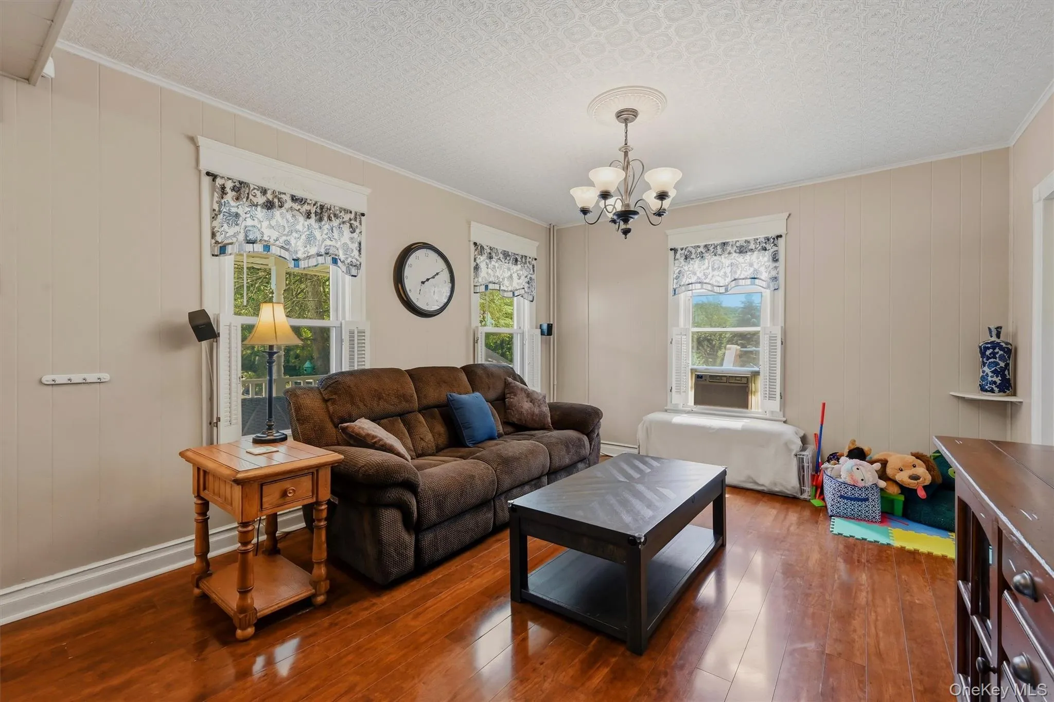 Living space featuring wood-finish flooring, vertical paneling, and two pane windows with white trim Living space featuring wood-finish flooring, vertical paneling, and two pane windows with white trim