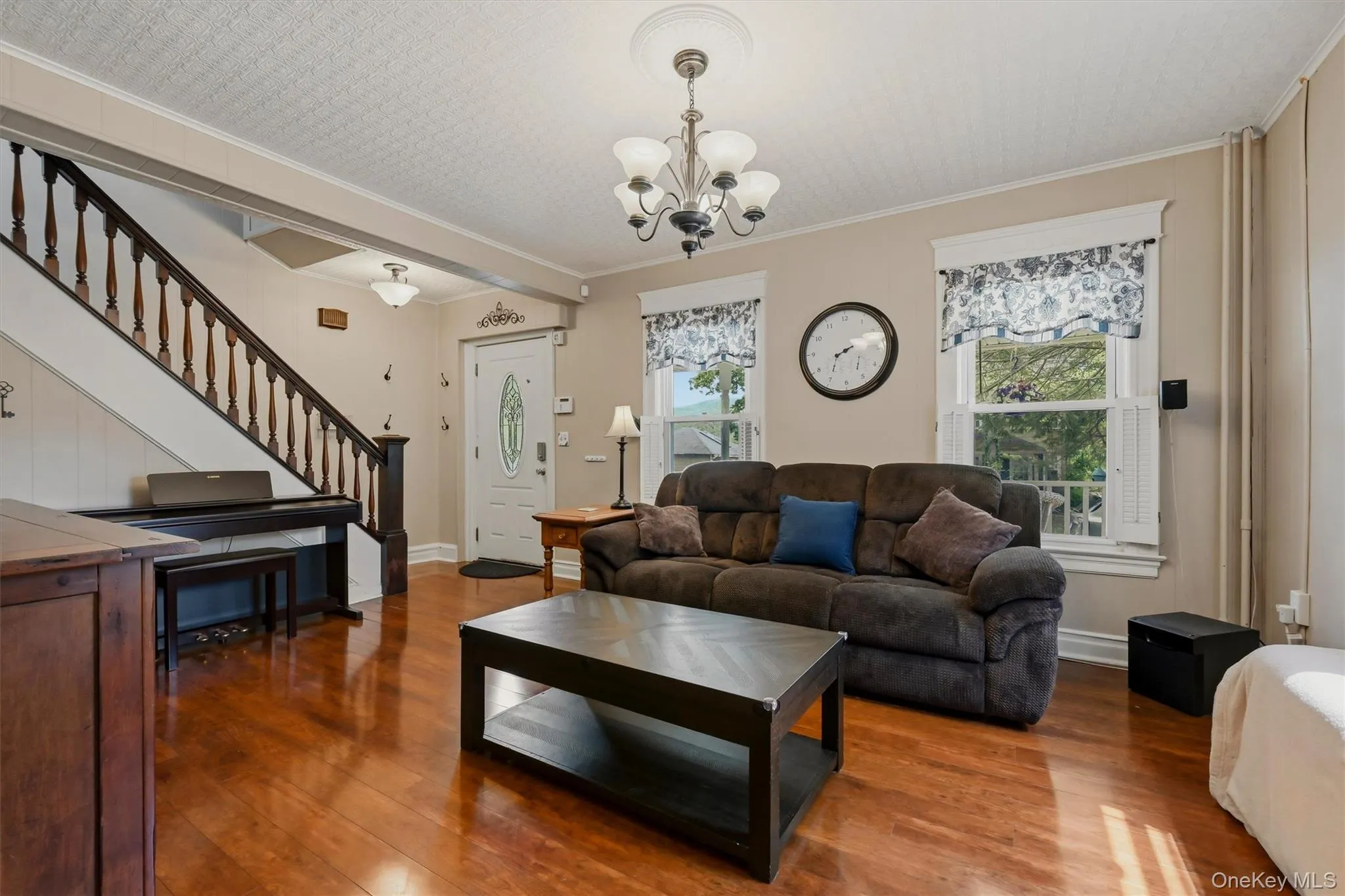 Hardwood flooring spans the main living area, complemented by a prominent staircase with dark wood banister and white risers Hardwood flooring spans the main living area, complemented by a prominent staircase with dark wood banister and white risers