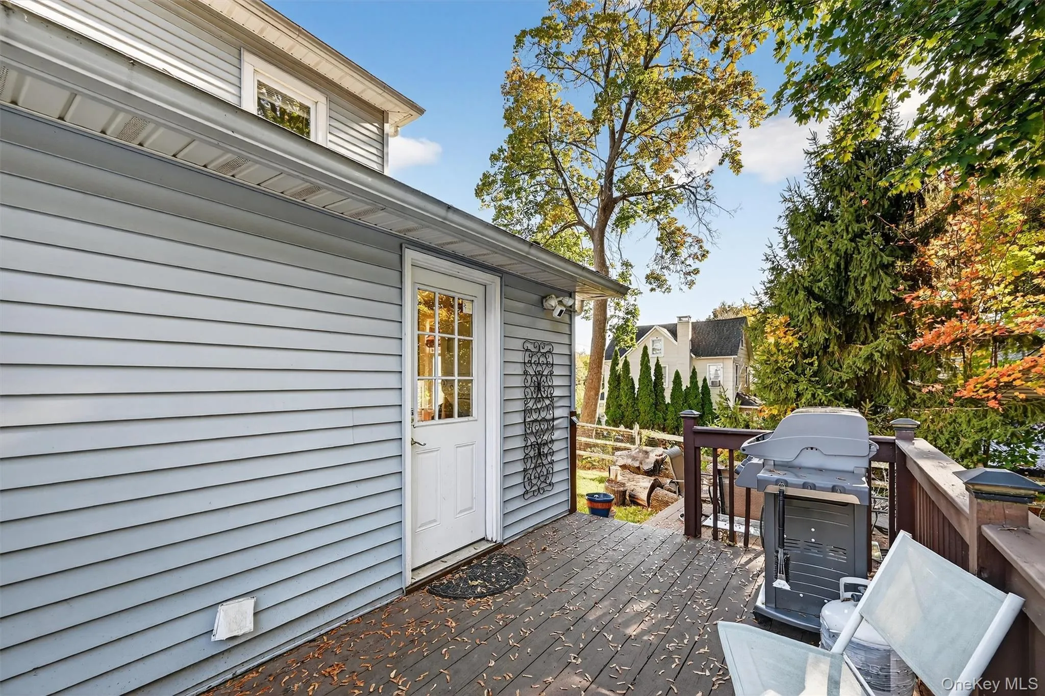 Wood-finish deck with a dark-stained railing, light gray siding, and a white door with glass panels Wood-finish deck with a dark-stained railing, light gray siding, and a white door with glass panels