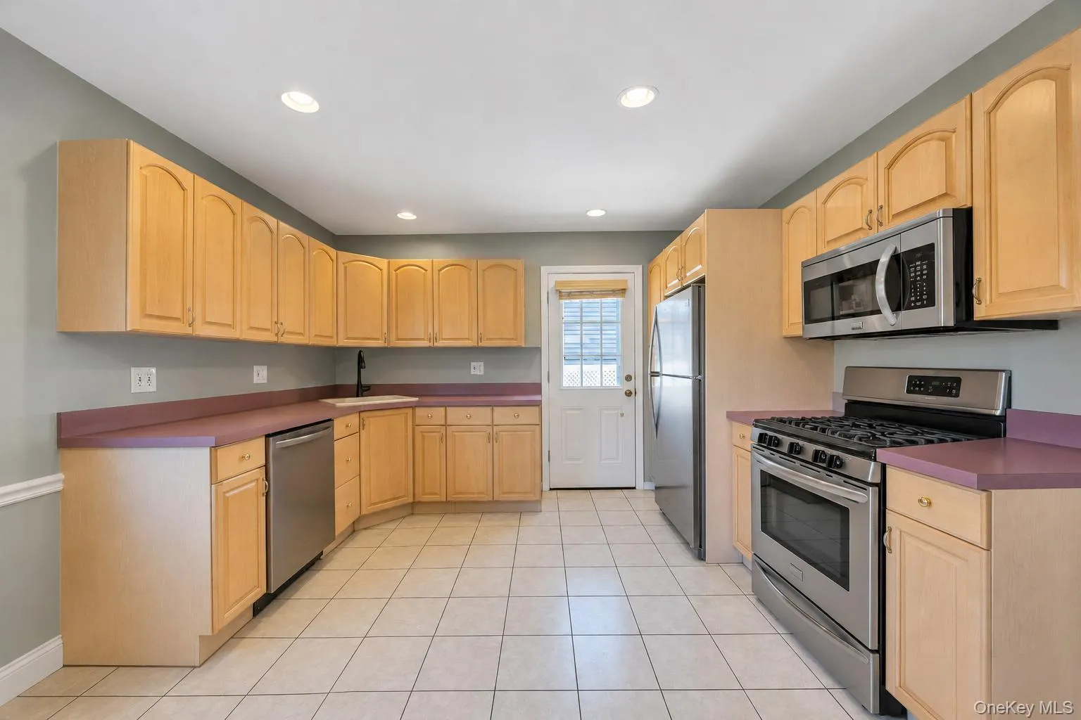 Kitchen featuring light wood cabinetry, stainless steel appliances, a tile floor, recessed lighting, and a rear exterior door Kitchen featuring light wood cabinetry, stainless steel appliances, a tile floor, recessed lighting, and a rear exterior door