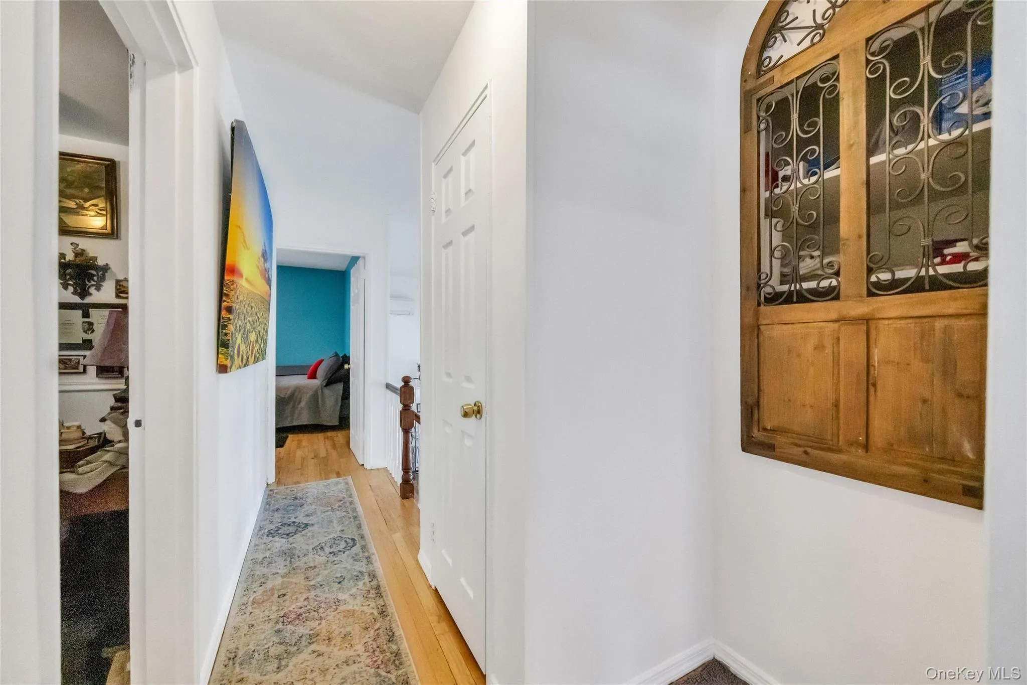 Hallway featuring wood-finish flooring, white walls, and an arched built-in wooden decorative window with wrought iron details Hallway featuring wood-finish flooring, white walls, and an arched built-in wooden decorative window with wrought iron details