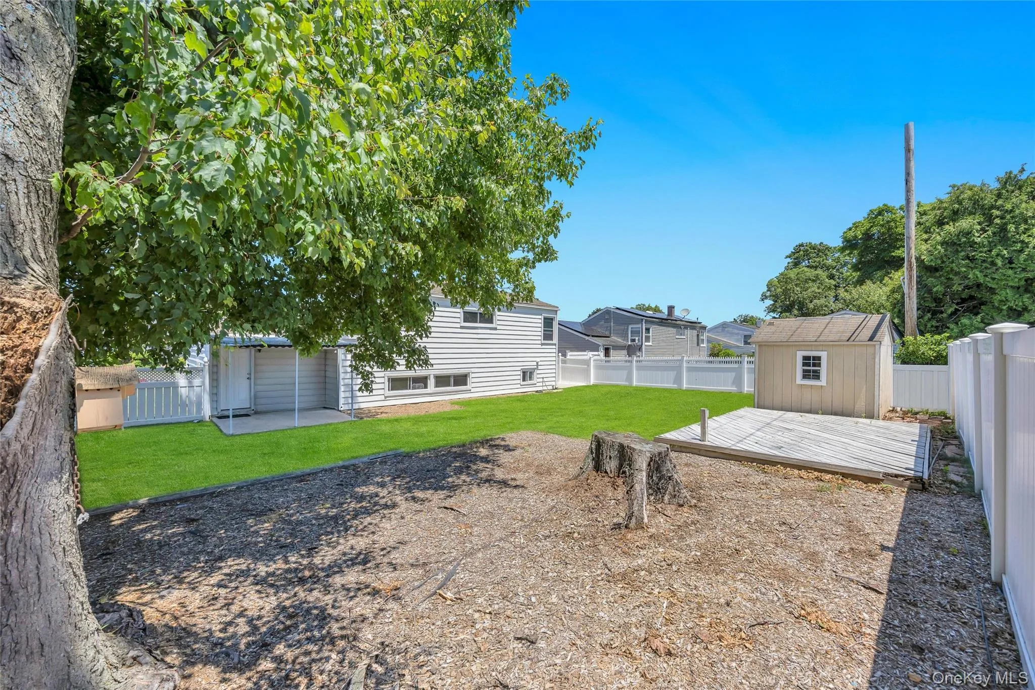Expansive outdoor space featuring a detached shed, a wooden deck platform, and a mature tree providing shade Expansive outdoor space featuring a detached shed, a wooden deck platform, and a mature tree providing shade