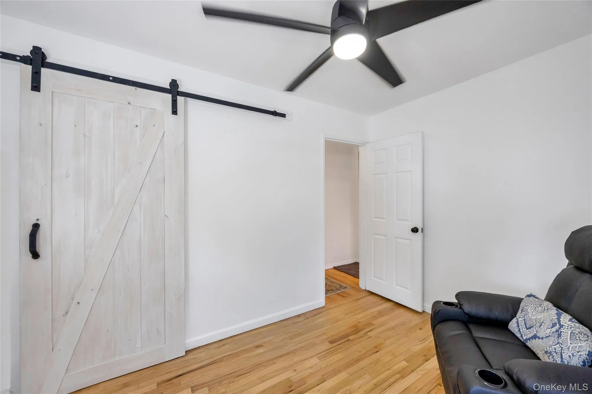 Room featuring a white barn door with black hardware, wood-finish flooring, and a contemporary ceiling fan with integrated lighting Room featuring a white barn door with black hardware, wood-finish flooring, and a contemporary ceiling fan with integrated lighting