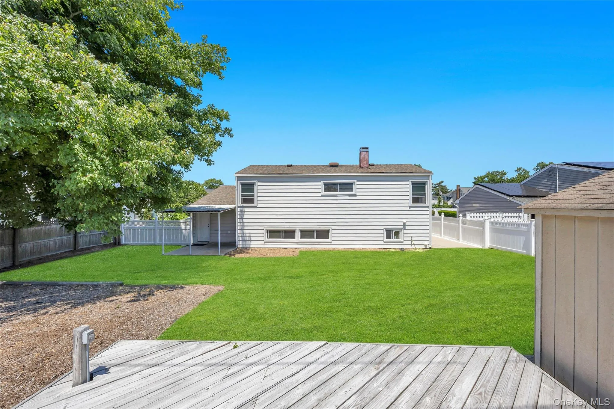 Expansive backyard featuring a manicured lawn, a partially covered patio, a detached storage shed, a wood fence, and a white privacy fence Expansive backyard featuring a manicured lawn, a partially covered patio, a detached storage shed, a wood fence, and a white privacy fence