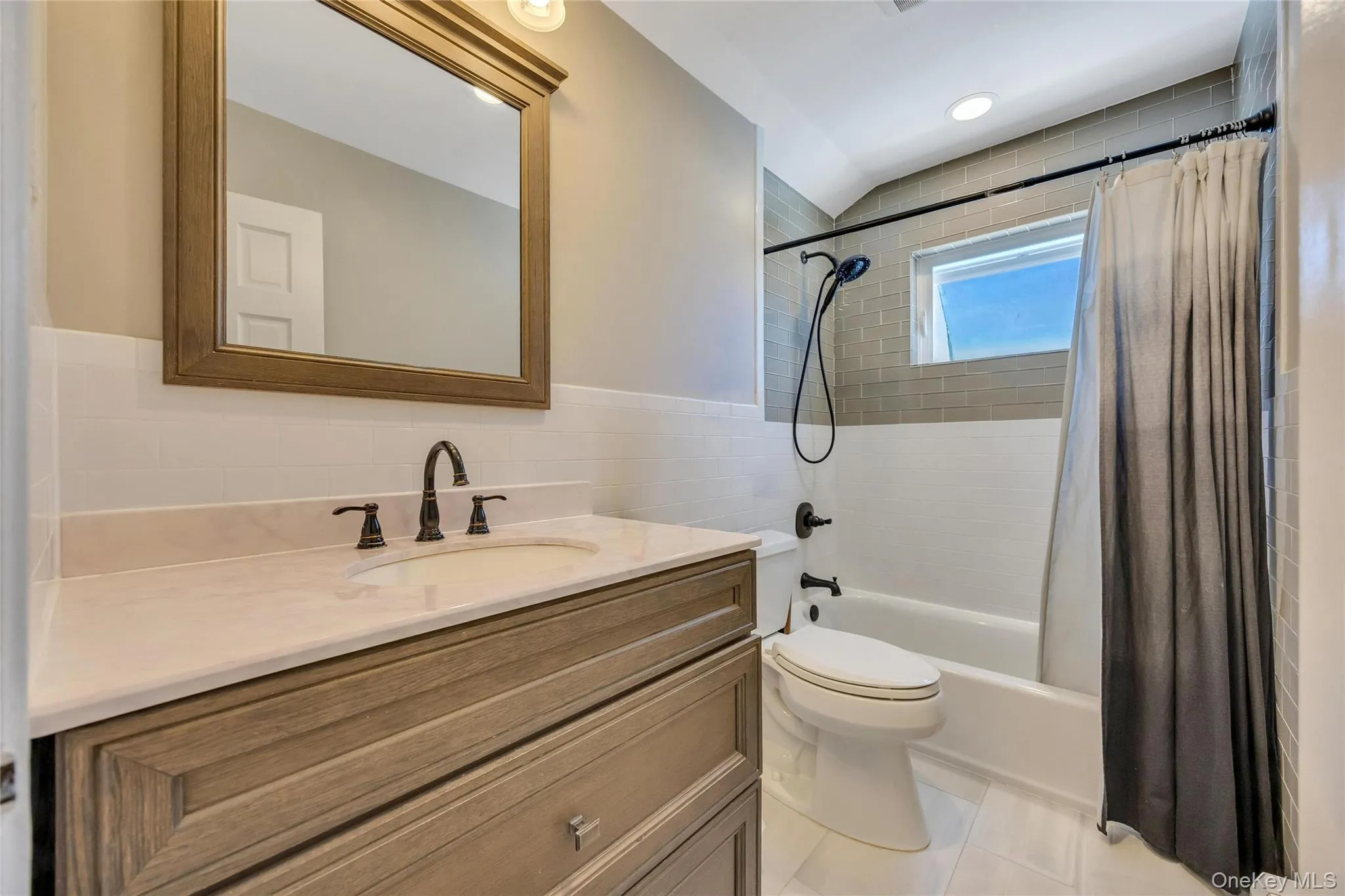 Bathroom featuring a light wood-finish vanity with an undermount sink, a light-toned countertop, and dark-finish fixtures Bathroom featuring a light wood-finish vanity with an undermount sink, a light-toned countertop, and dark-finish fixtures
