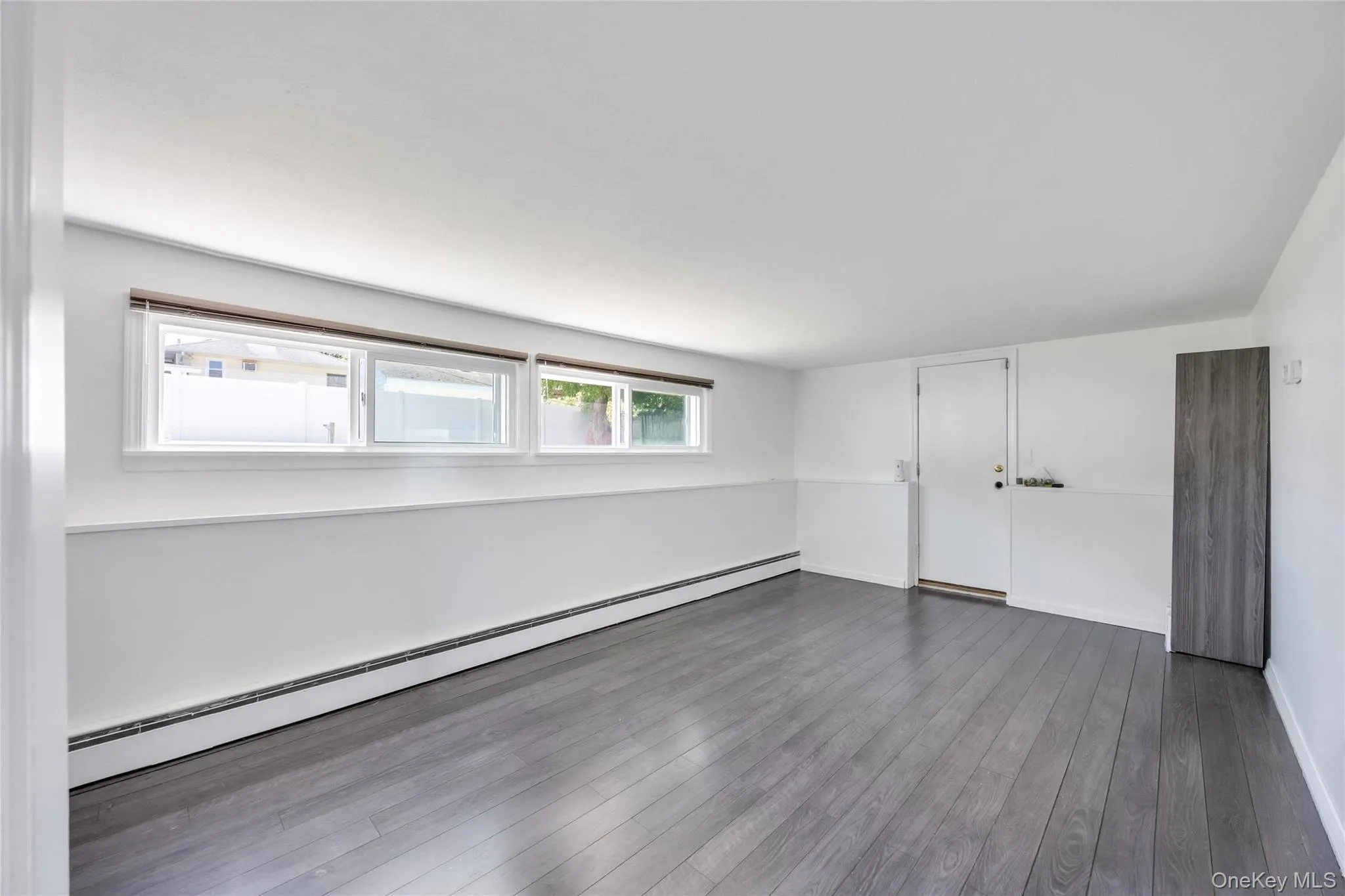 Spacious room featuring dark wood-finish flooring, white walls, and a white wainscoting detail Spacious room featuring dark wood-finish flooring, white walls, and a white wainscoting detail