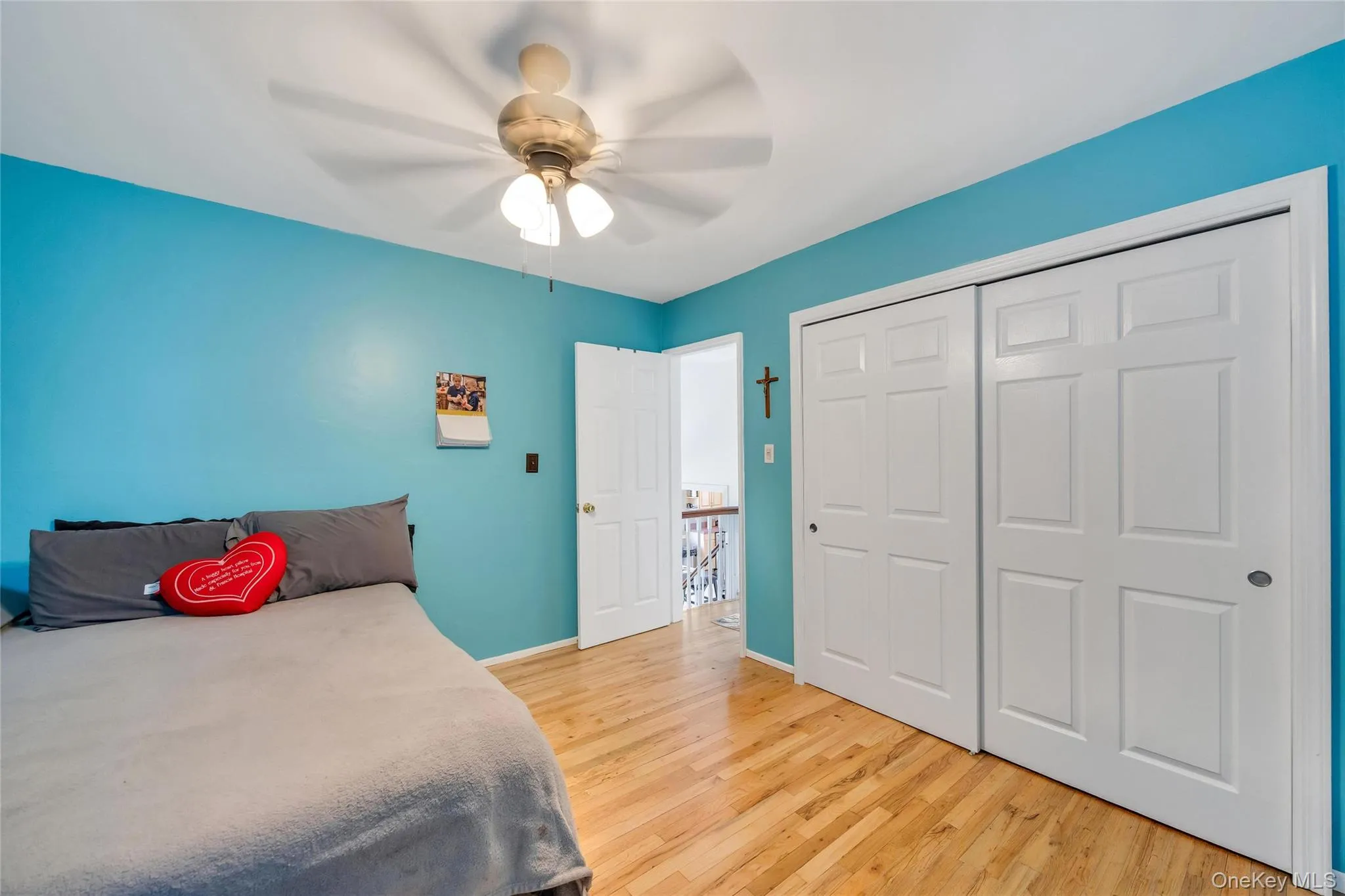 Room featuring wood-finish flooring, a ceiling fan with integrated lighting, and a double bi-fold closet with panel doors Room featuring wood-finish flooring, a ceiling fan with integrated lighting, and a double bi-fold closet with panel doors
