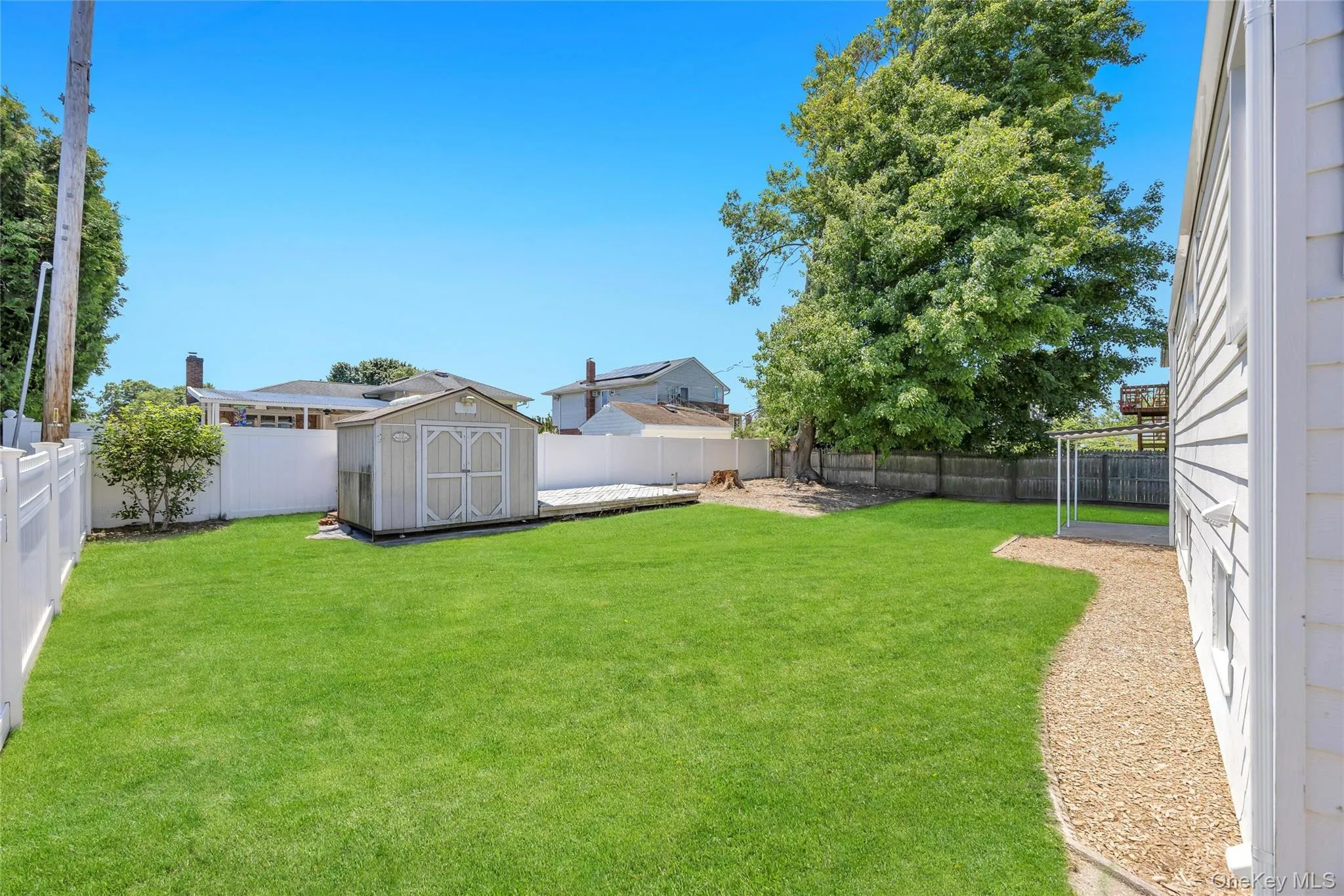 Expansive lawn area featuring a storage shed, white vinyl fencing, and a gravel pathway Expansive lawn area featuring a storage shed, white vinyl fencing, and a gravel pathway