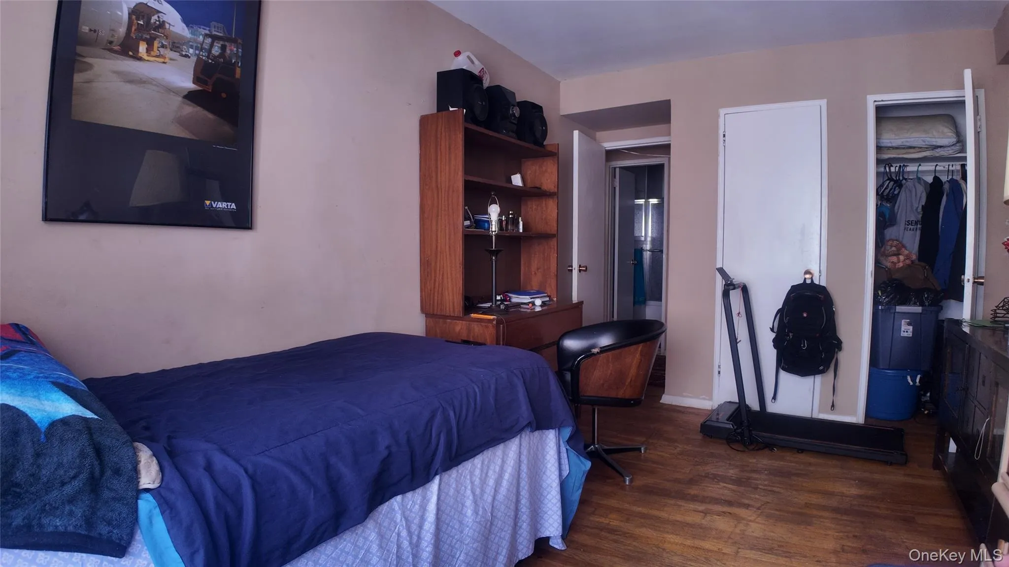 Interior room featuring wood-finish flooring, a wall-mounted television, and a built-in closet with an open door Interior room featuring wood-finish flooring, a wall-mounted television, and a built-in closet with an open door