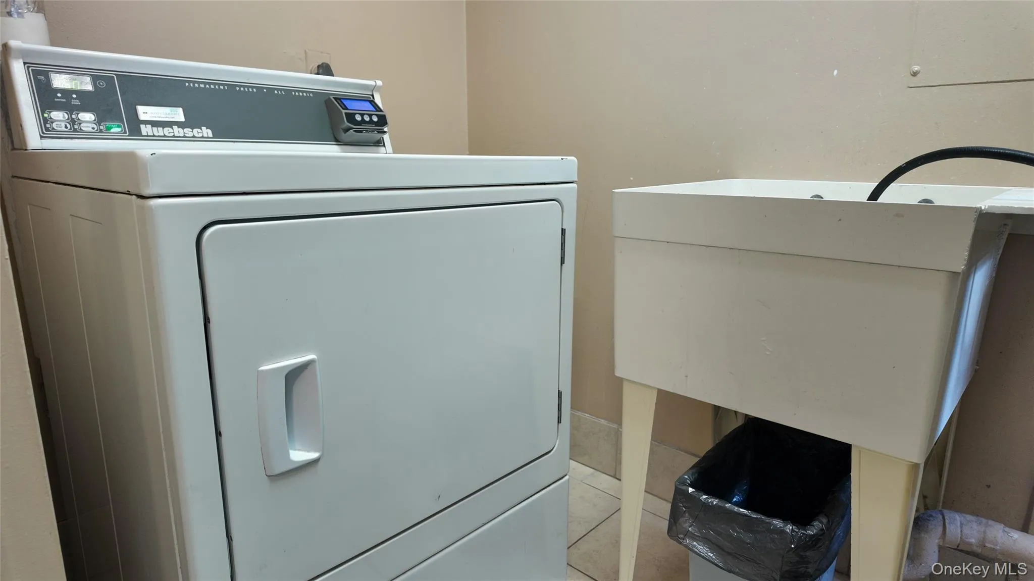Dedicated laundry area featuring a white front-load dryer and a utility sink with a black hose Dedicated laundry area featuring a white front-load dryer and a utility sink with a black hose