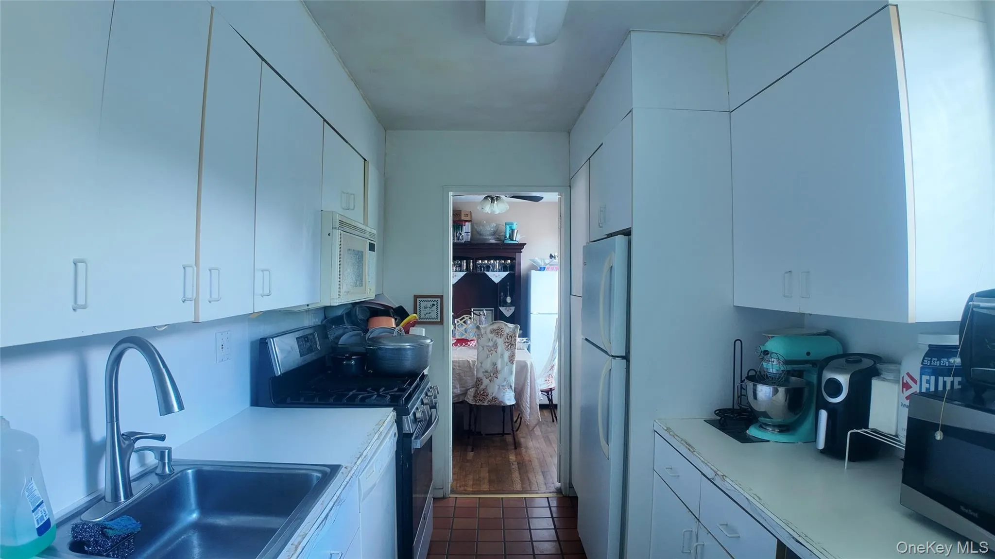Galley kitchen featuring white cabinetry, a stainless steel sink, gas range, and a built-in microwave Galley kitchen featuring white cabinetry, a stainless steel sink, gas range, and a built-in microwave