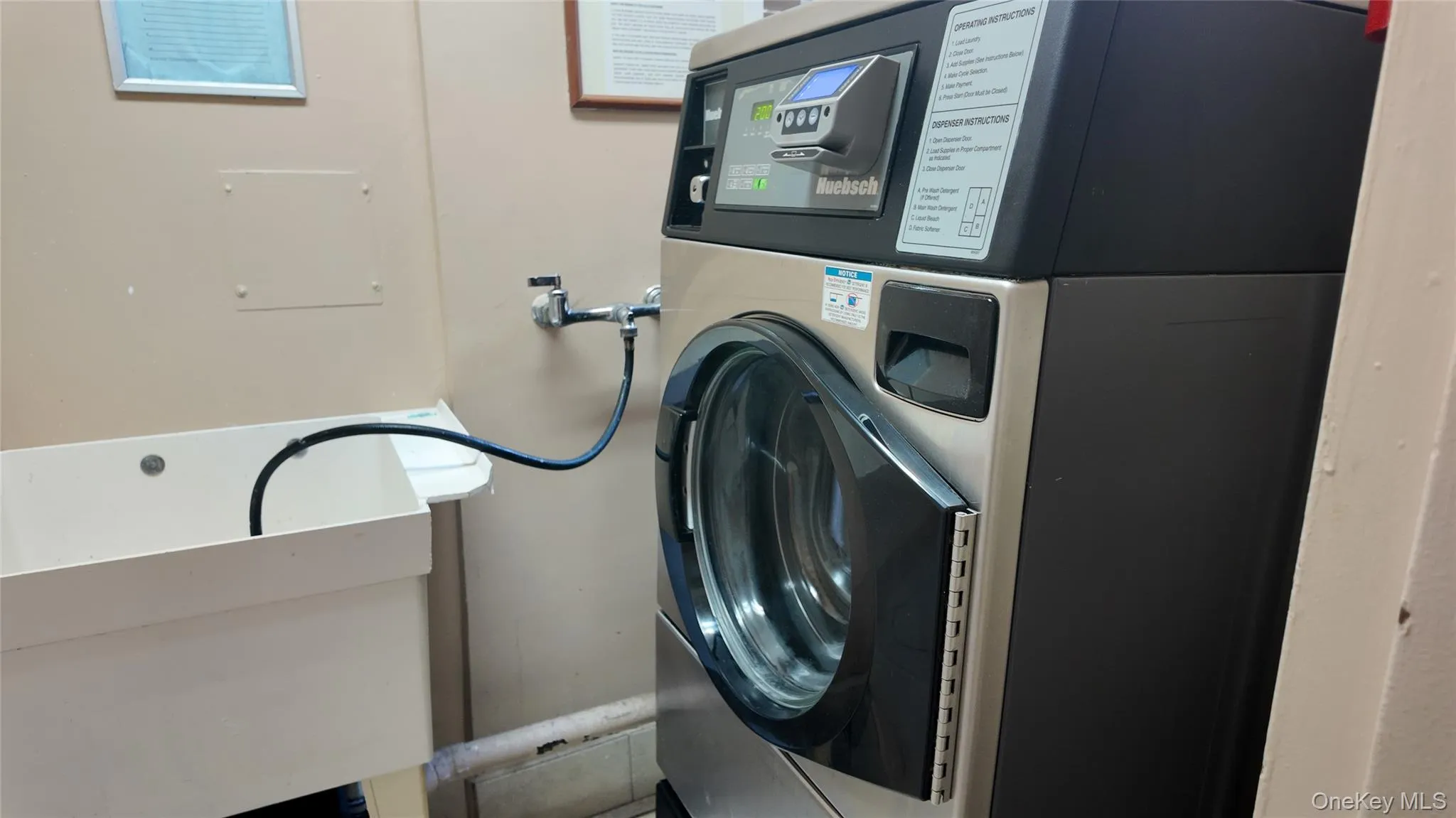 Front-loading washing machine with a stainless steel drum and digital display, paired with a white utility sink and wall-mounted faucet Front-loading washing machine with a stainless steel drum and digital display, paired with a white utility sink and wall-mounted faucet