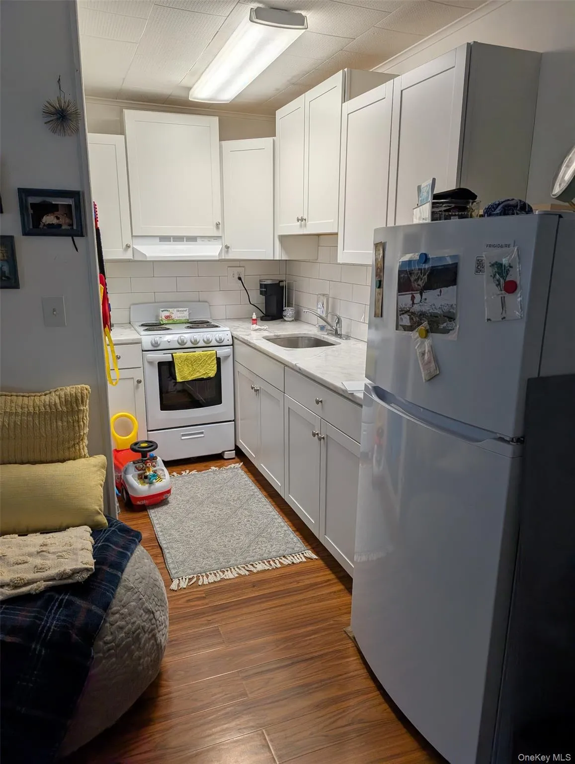 Kitchen featuring white appliances, premium range hood, a sink, wood finished floors, and backsplash Kitchen featuring white appliances, premium range hood, a sink, wood finished floors, and backsplash