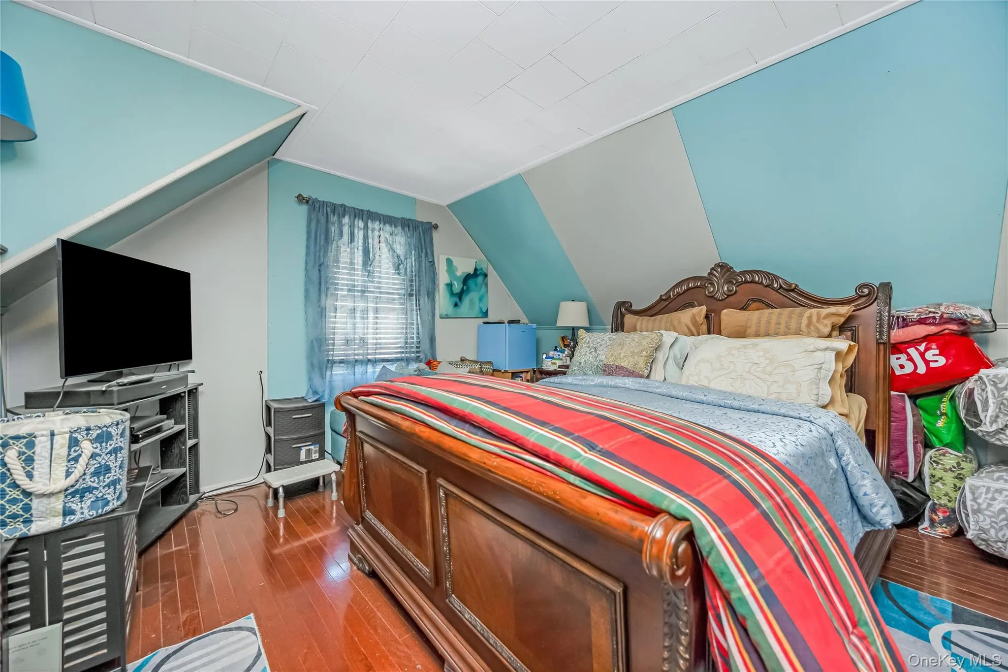 Bedroom featuring wood-finish flooring, sloped ceilings, and a window with blinds Bedroom featuring wood-finish flooring, sloped ceilings, and a window with blinds