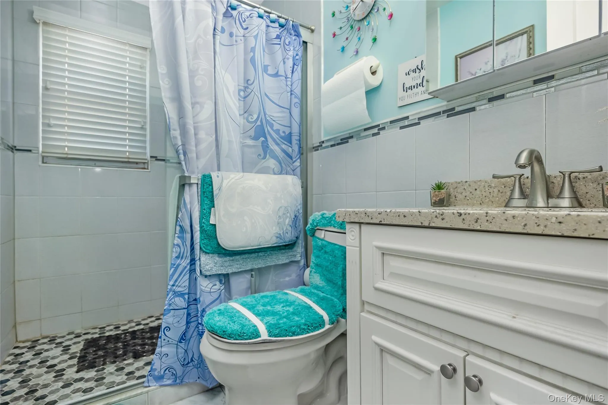 Bathroom featuring a glass-enclosed shower with mosaic tile flooring and a window with horizontal blinds Bathroom featuring a glass-enclosed shower with mosaic tile flooring and a window with horizontal blinds