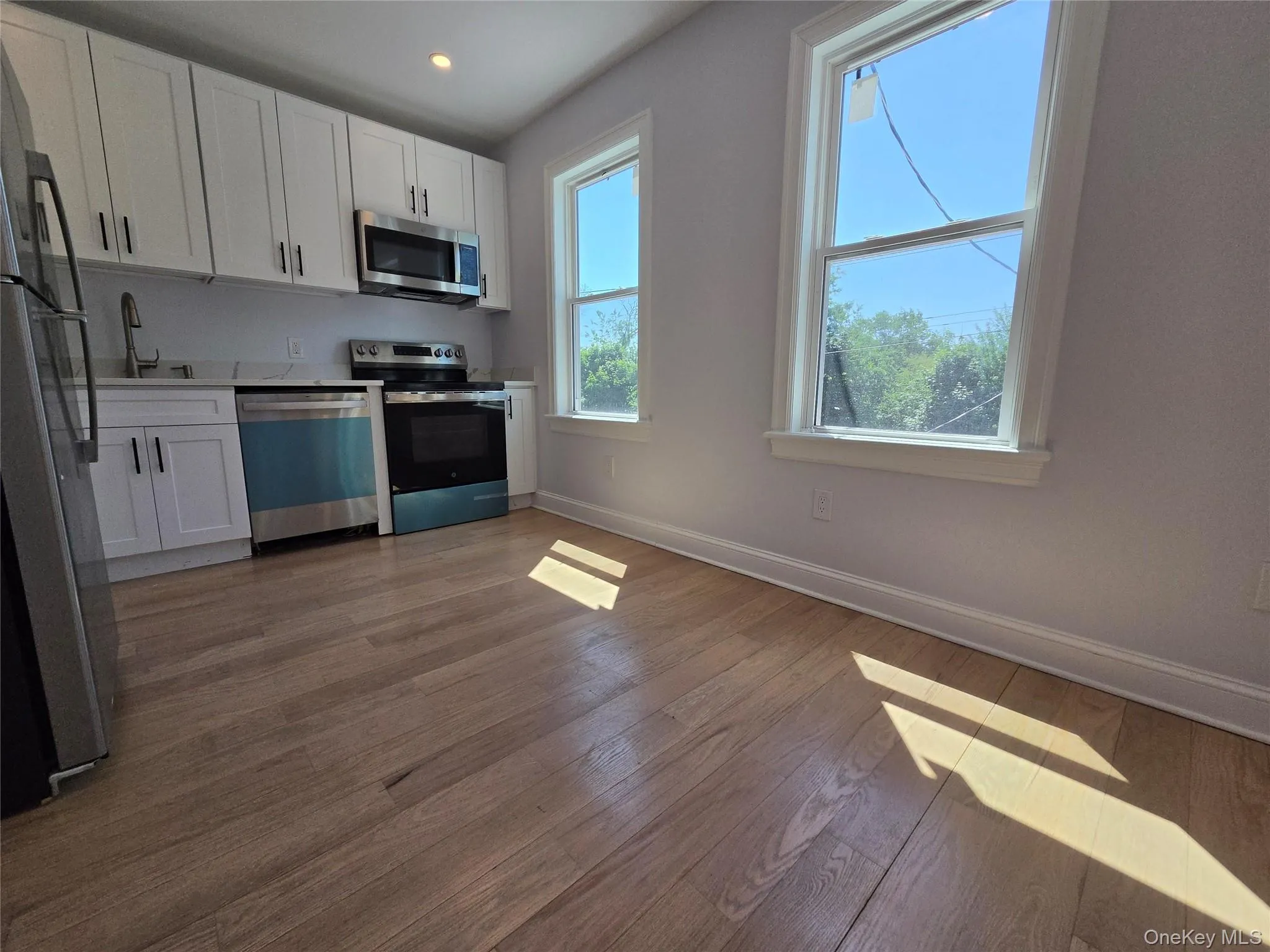Modern kitchen featuring white shaker-style cabinetry, stainless steel appliances, and a light-toned wood-finish floor Modern kitchen featuring white shaker-style cabinetry, stainless steel appliances, and a light-toned wood-finish floor