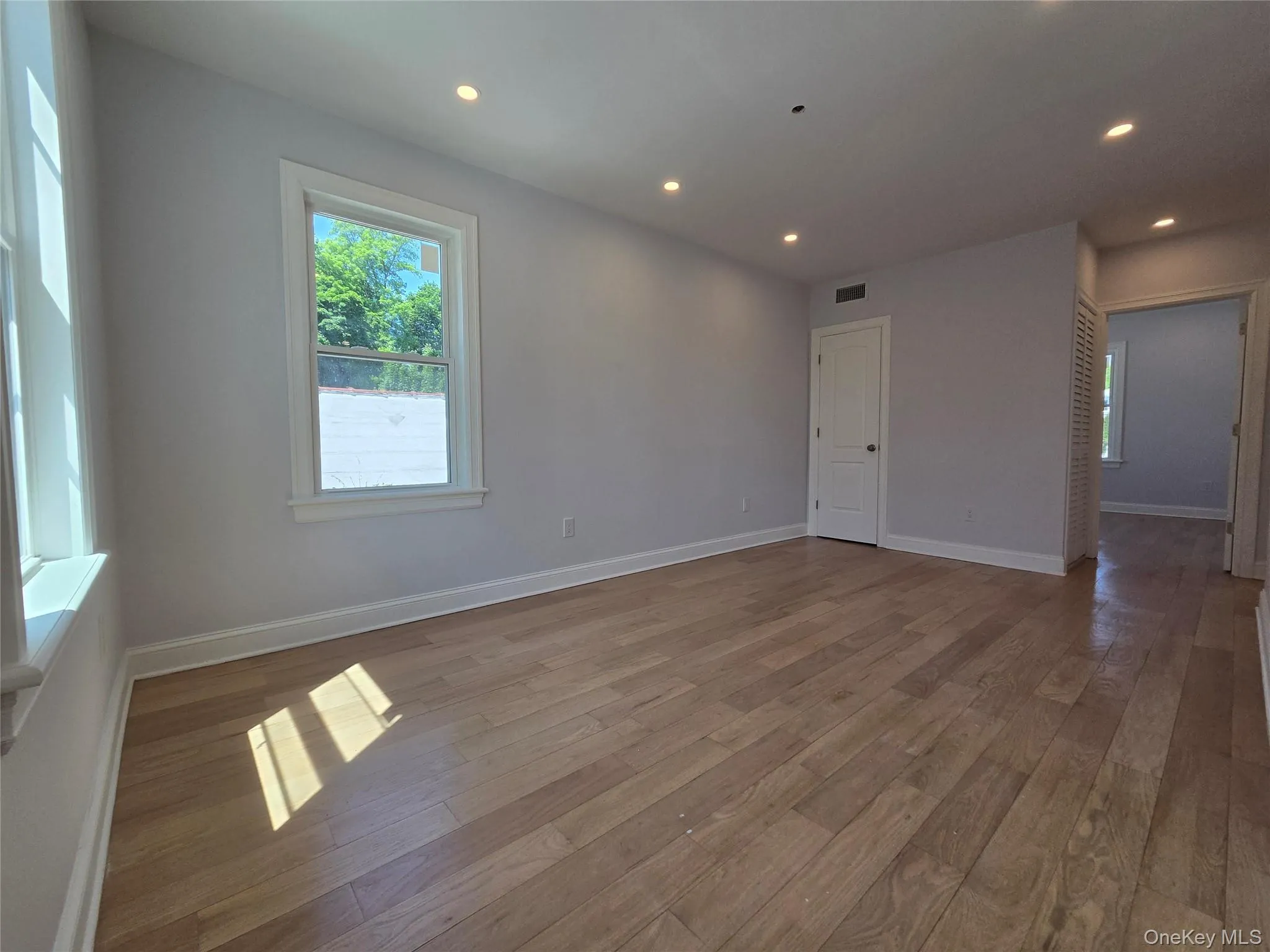 Spacious room featuring light wood-finish flooring, recessed lighting, multiple windows with white trim, a white interior door, and light gray wall paint Spacious room featuring light wood-finish flooring, recessed lighting, multiple windows with white trim, a white interior door, and light gray wall paint