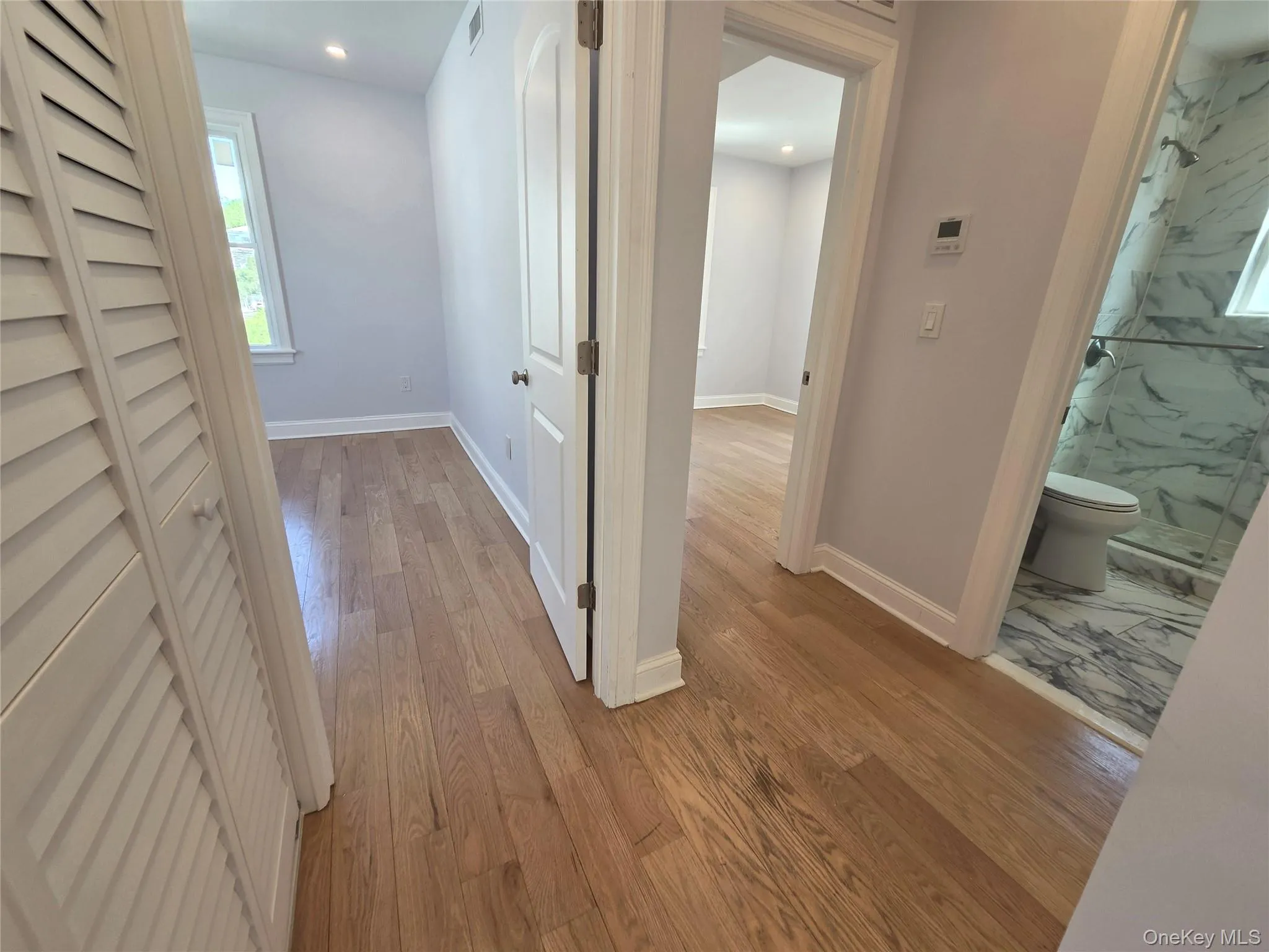 Hallway featuring wood-finish flooring, white trim, and light-toned walls Hallway featuring wood-finish flooring, white trim, and light-toned walls