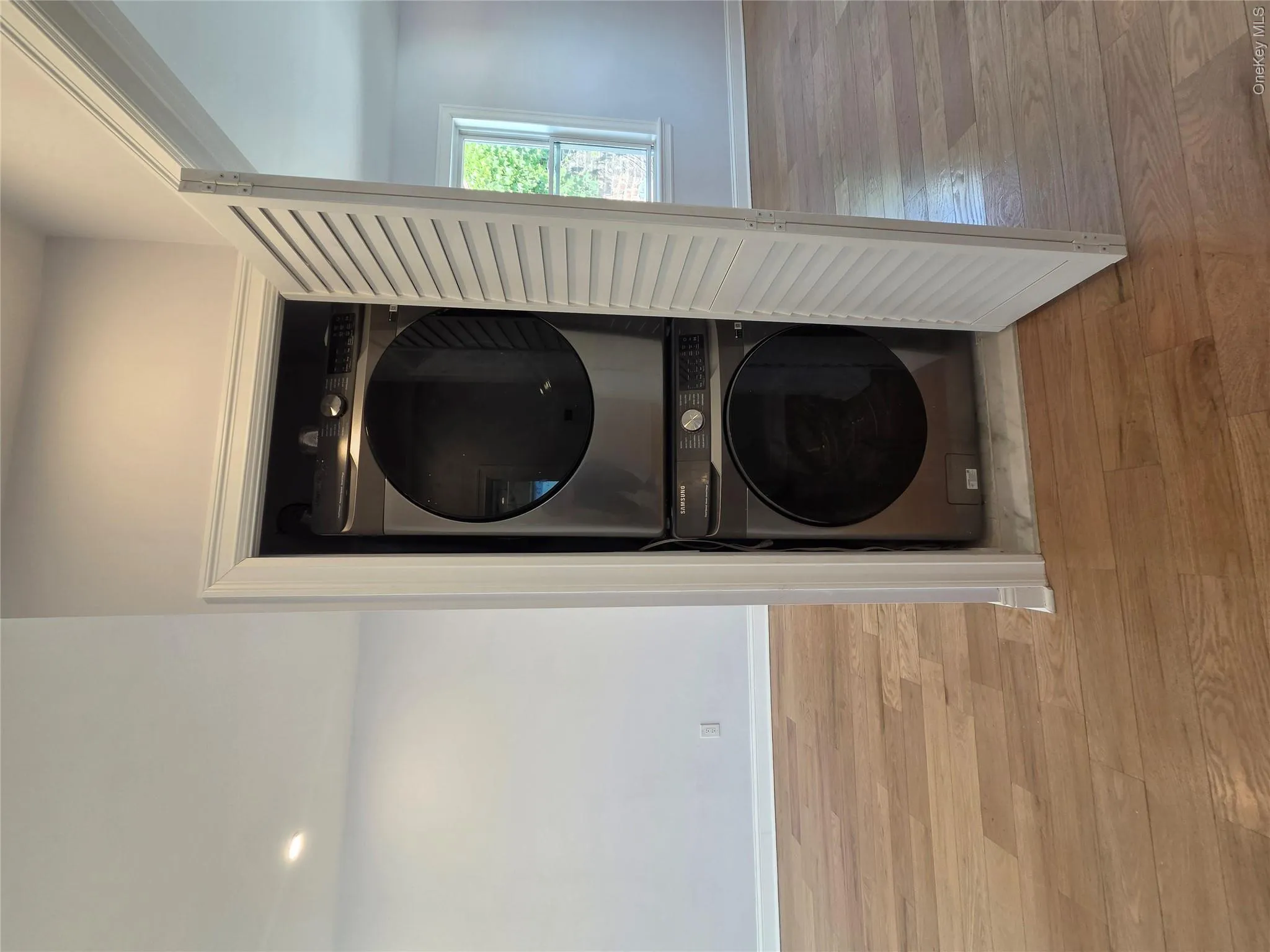 Integrated stacked washer and dryer in a louvered bi-fold closet, featuring wood-finish flooring Integrated stacked washer and dryer in a louvered bi-fold closet, featuring wood-finish flooring