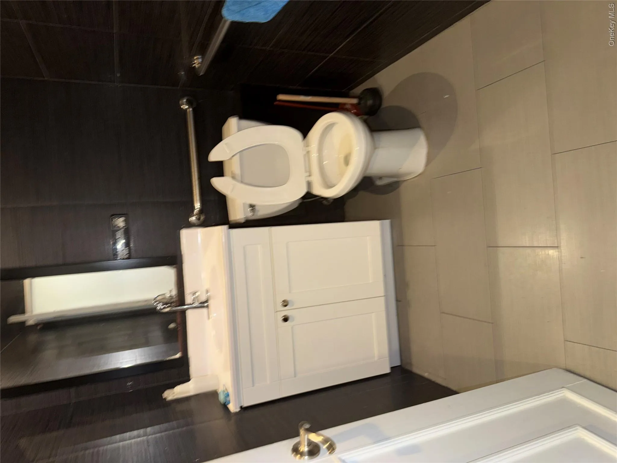 Contemporary bathroom featuring dark horizontal wall tiling, a white vanity with double doors and a countertop sink, a wall-mounted mirror, and a toilet Contemporary bathroom featuring dark horizontal wall tiling, a white vanity with double doors and a countertop sink, a wall-mounted mirror, and a toilet