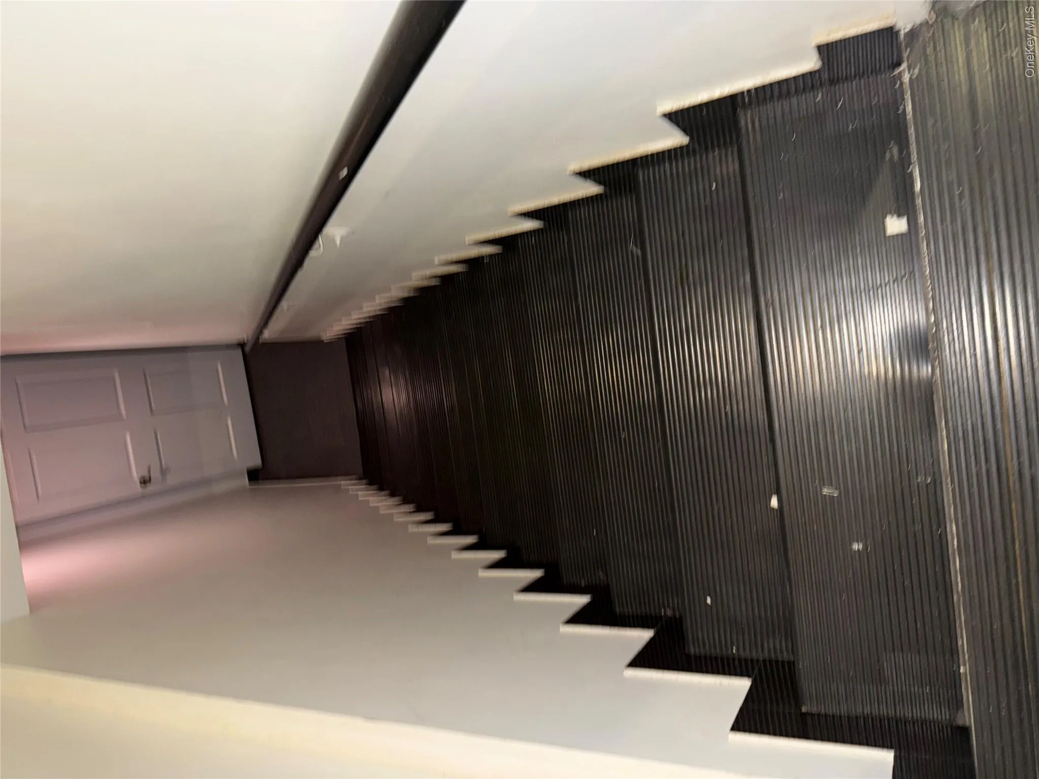 Staircase featuring dark tread covers, a contrasting white wall, and a black handrail Staircase featuring dark tread covers, a contrasting white wall, and a black handrail